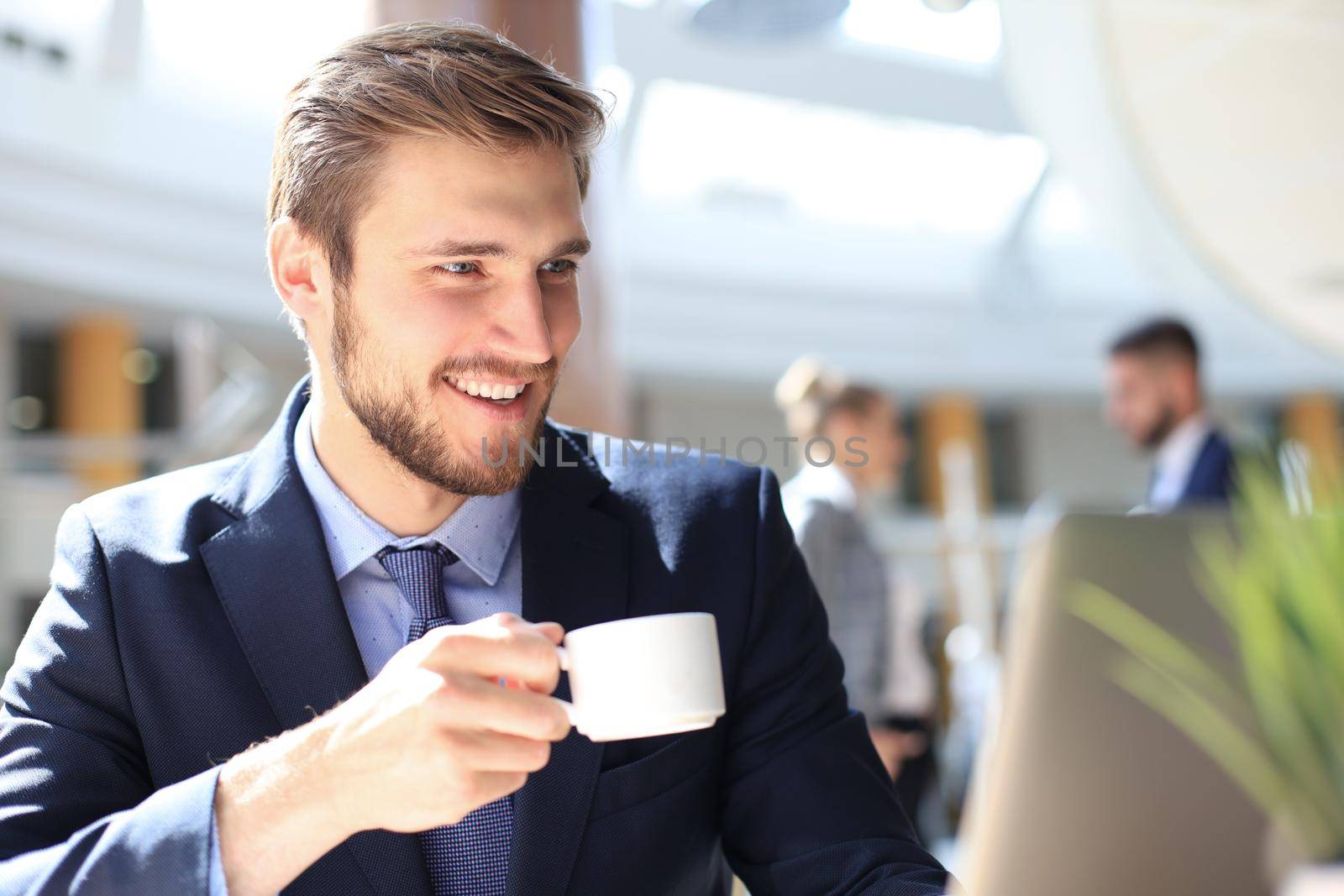 young businessman drinking coffee in office while typing on computer
