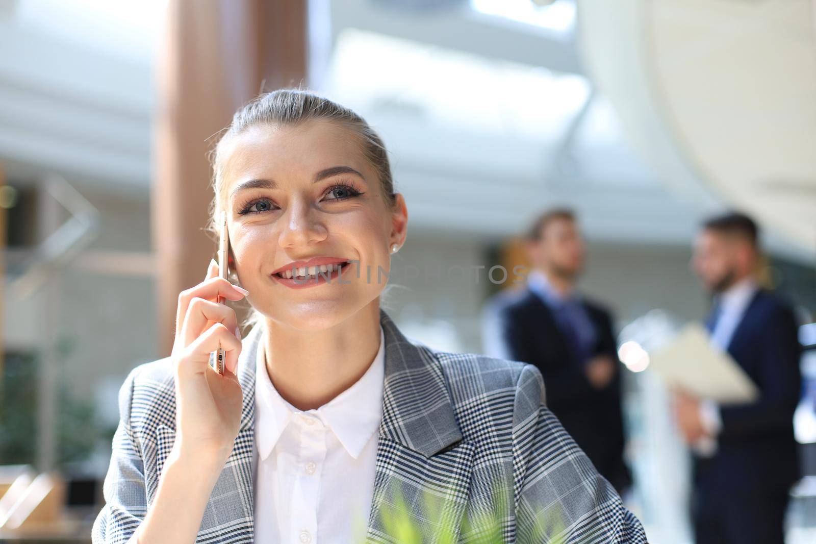 Young smiling business woman using smartphone near computer in office