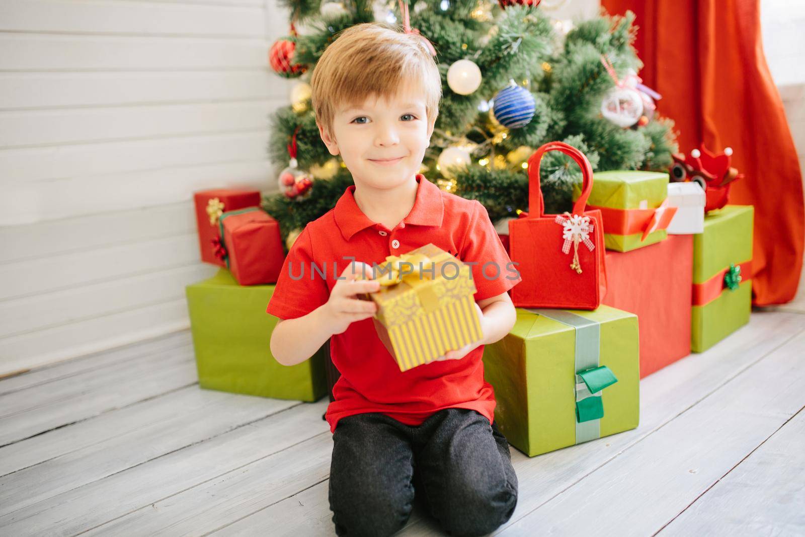Cute little boy of about five year with a gift in a decorated Christmas room with a xmas tree. .