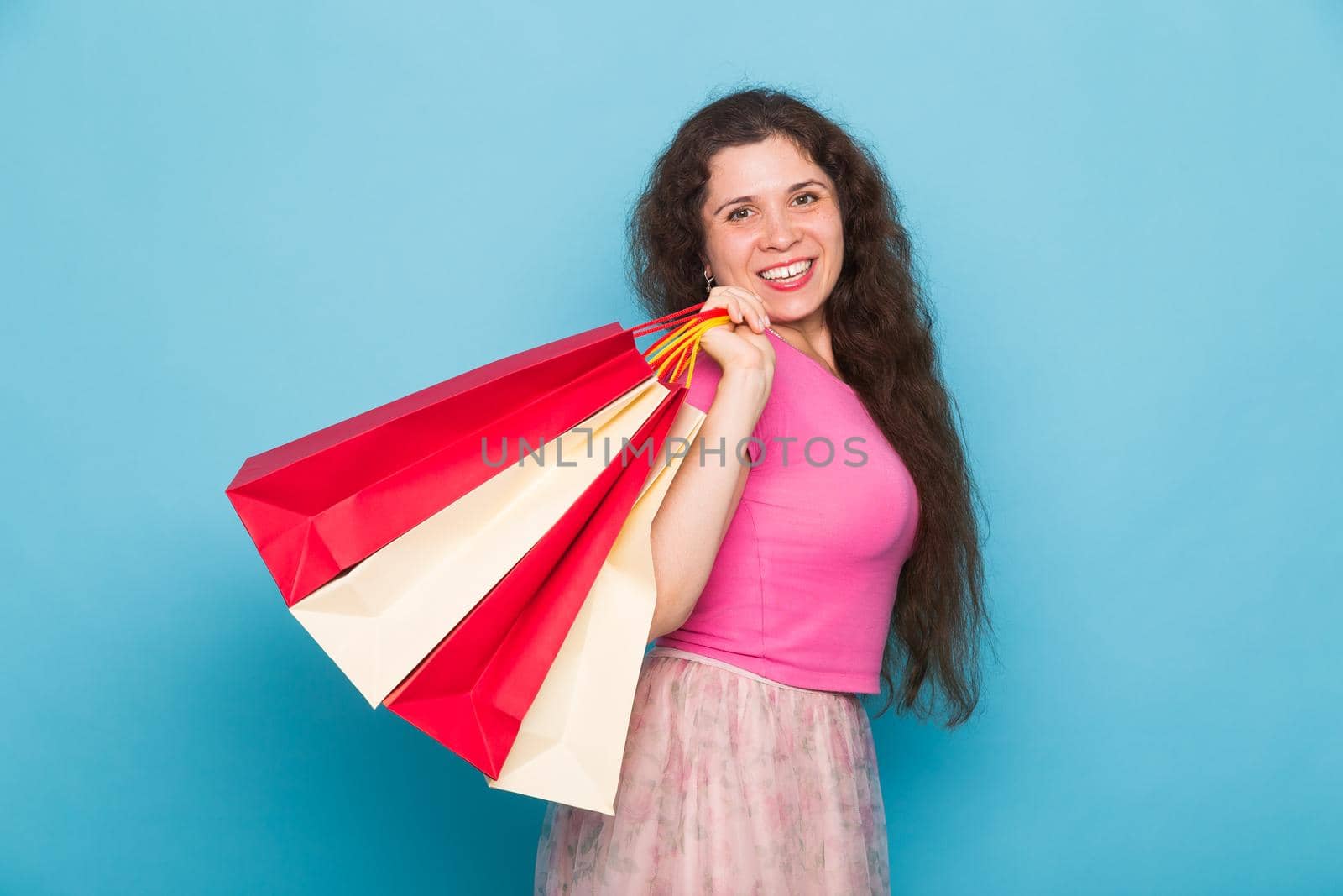 Portrait of young happy smiling woman with shopping bags, over blue background. Purchase, sale and people concept.