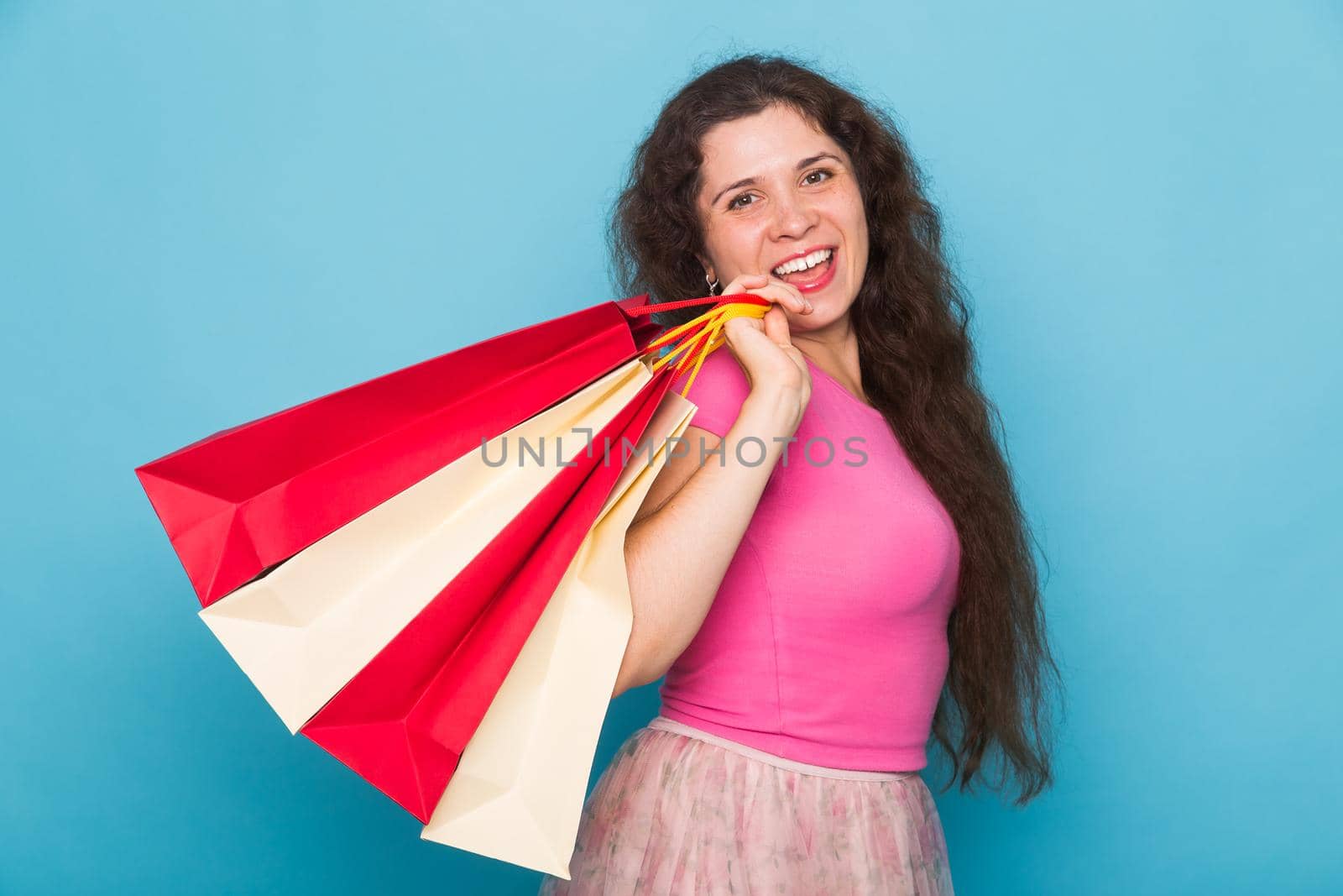 Portrait of young happy smiling woman with shopping bags, over blue background. Purchase, sale and people concept by Satura86