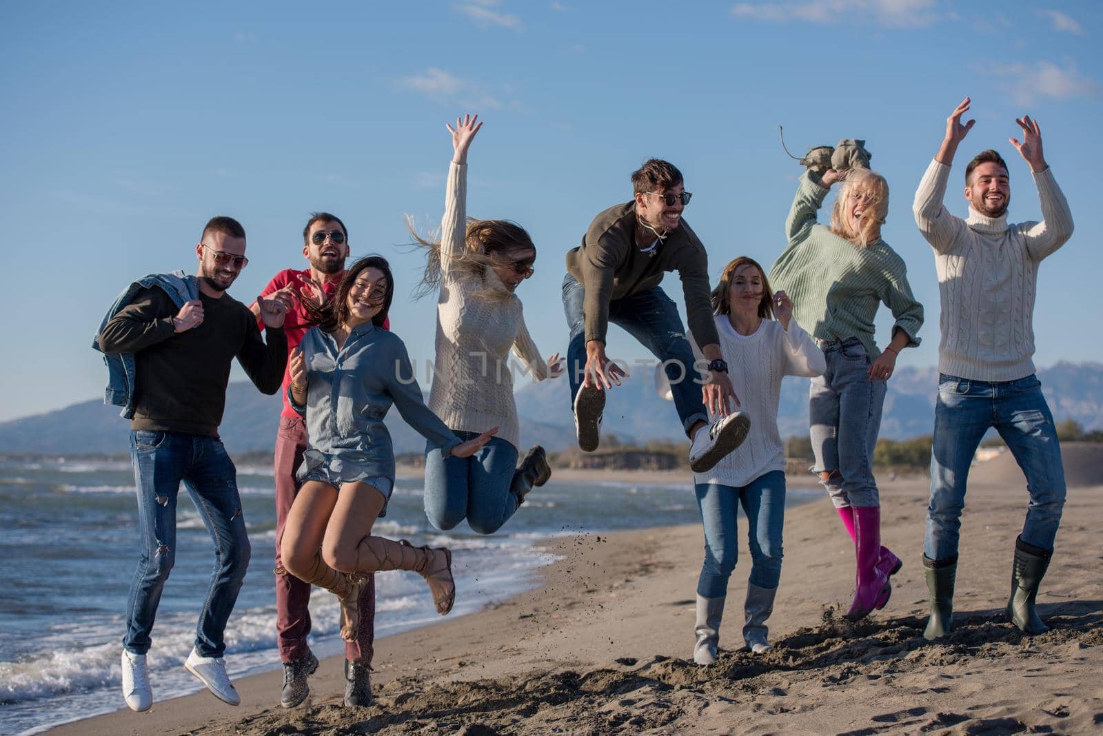 Group of excited young friends jumping together at sunny autumn beach