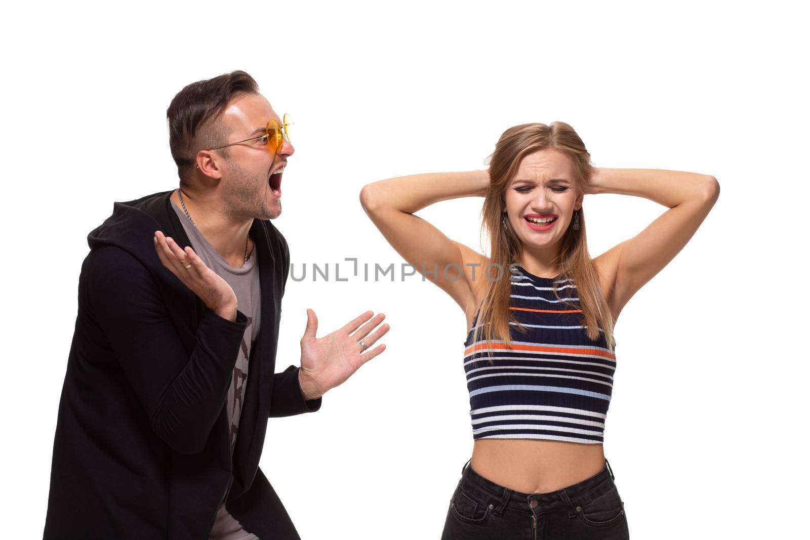 Young emotional man and woman quarrel. Man screaming at the woman waving her arms, the girl covered her ears on white background