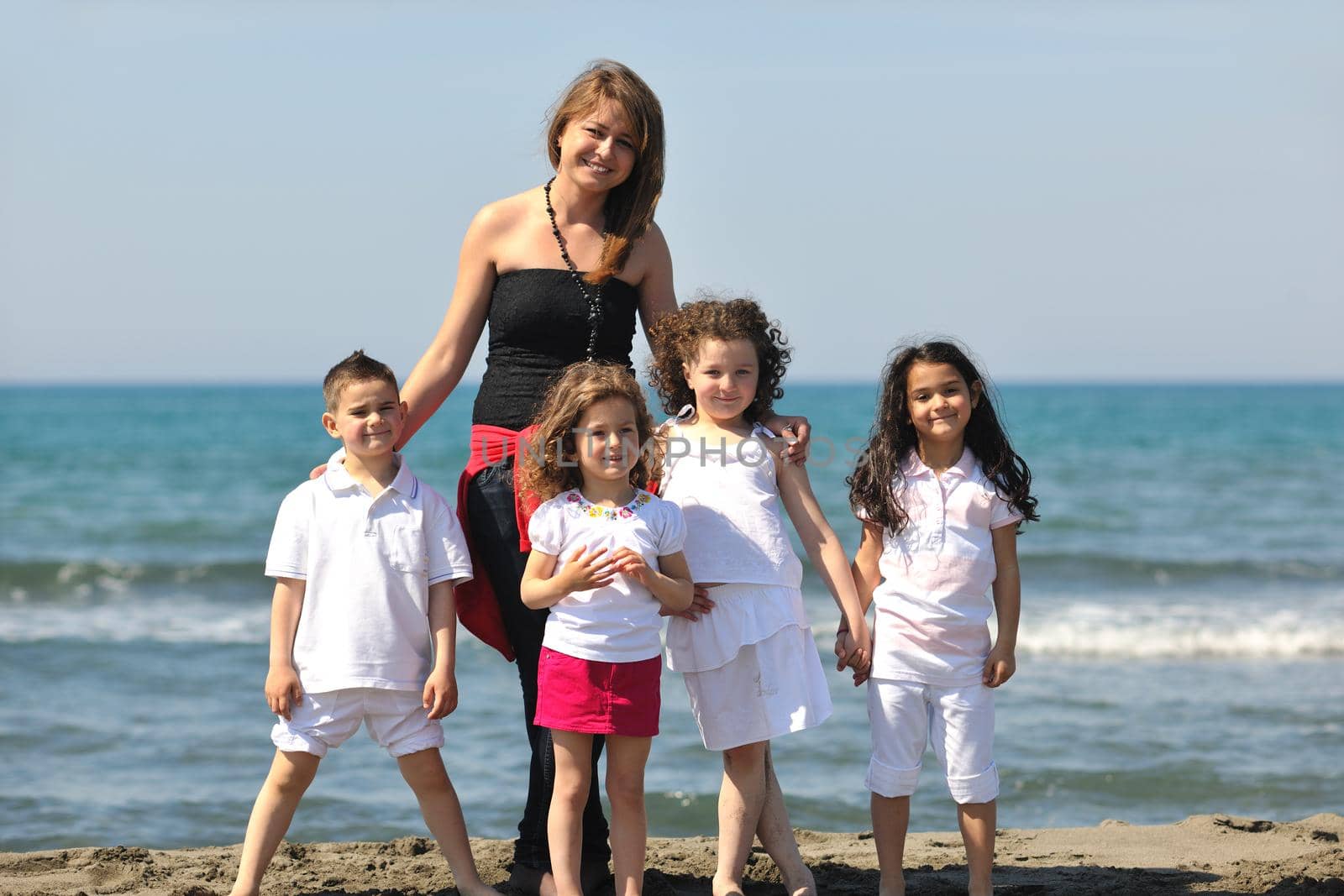 group portrait of happy childrens with young female  teacher on beach