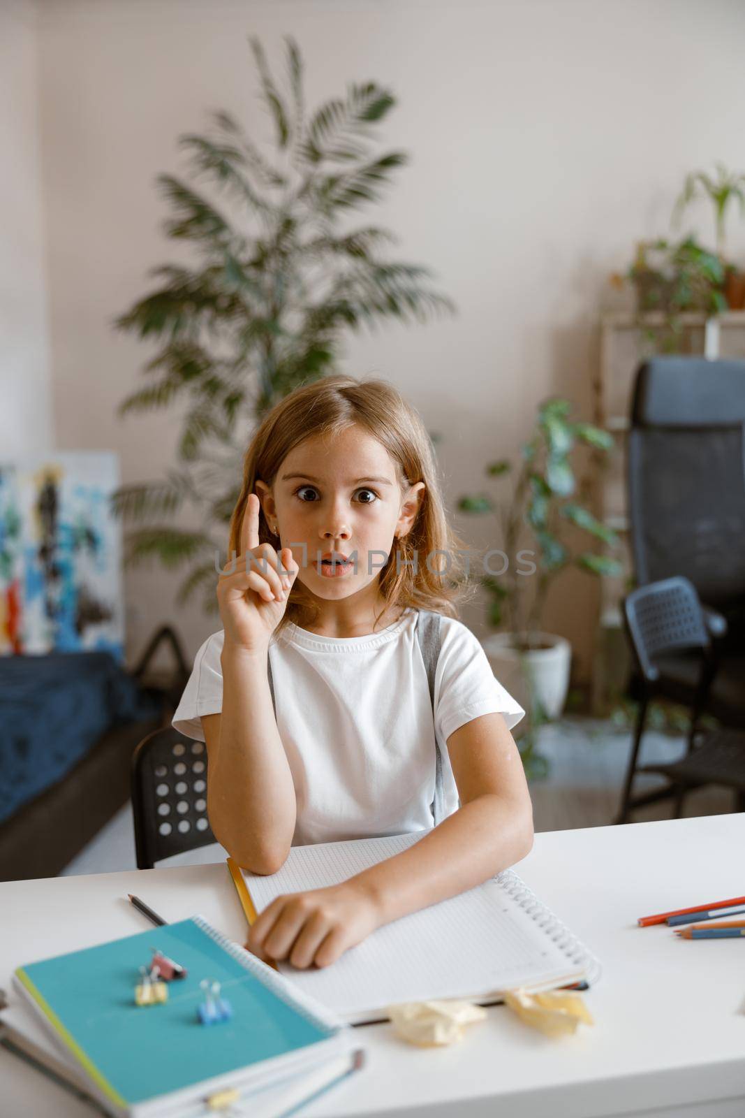 Funny little girl got idea at desk with supplies in light room by friendsstock