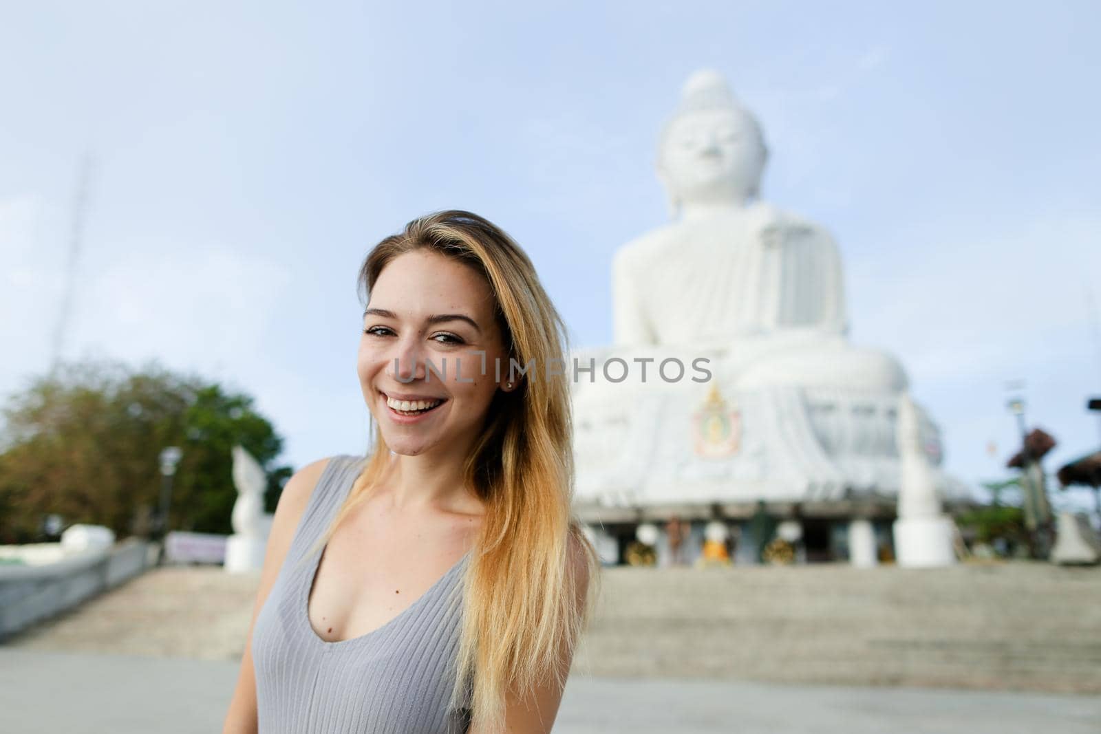 Young blonde girl standing with Buddha statue in Phuket, Thailand. Concept of traveling to Asia and buddhism landmark.