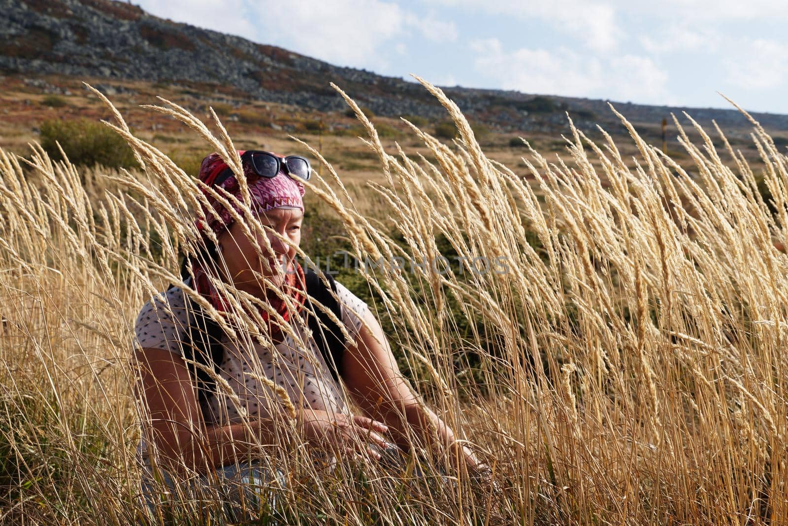 portrait of a woman in tall dry grass against a background of mountains by Annado