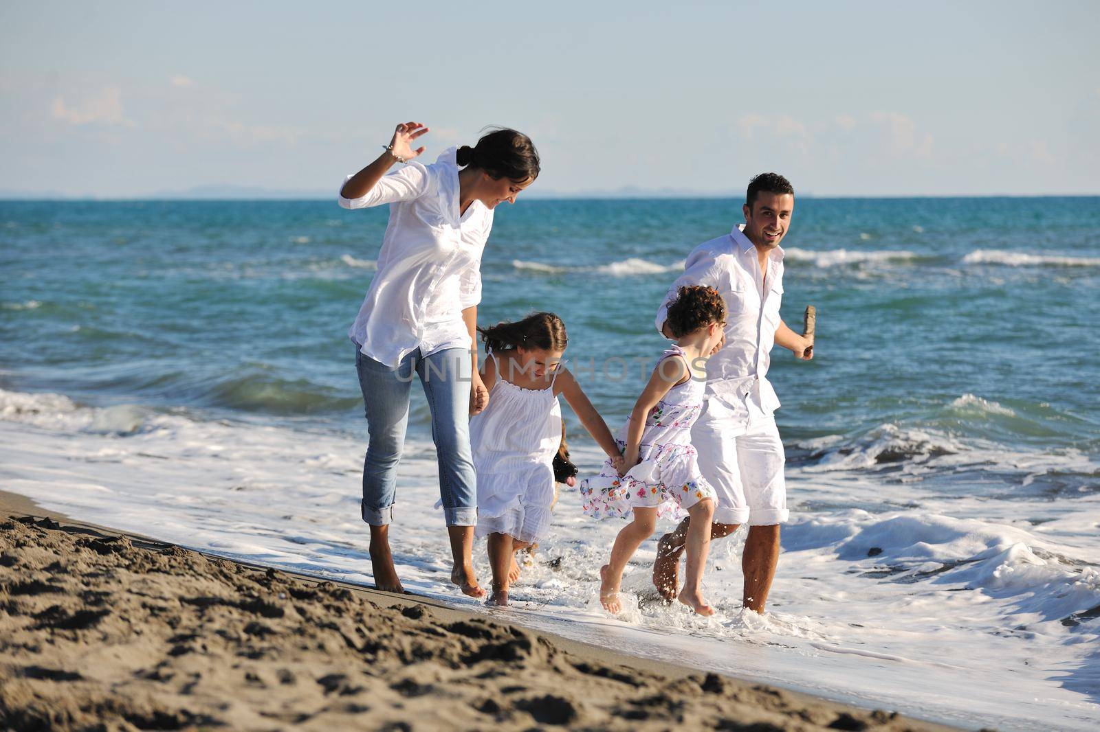 happy young family in white clothing have fun and play with beautiful dog at vacations on beautiful beach 