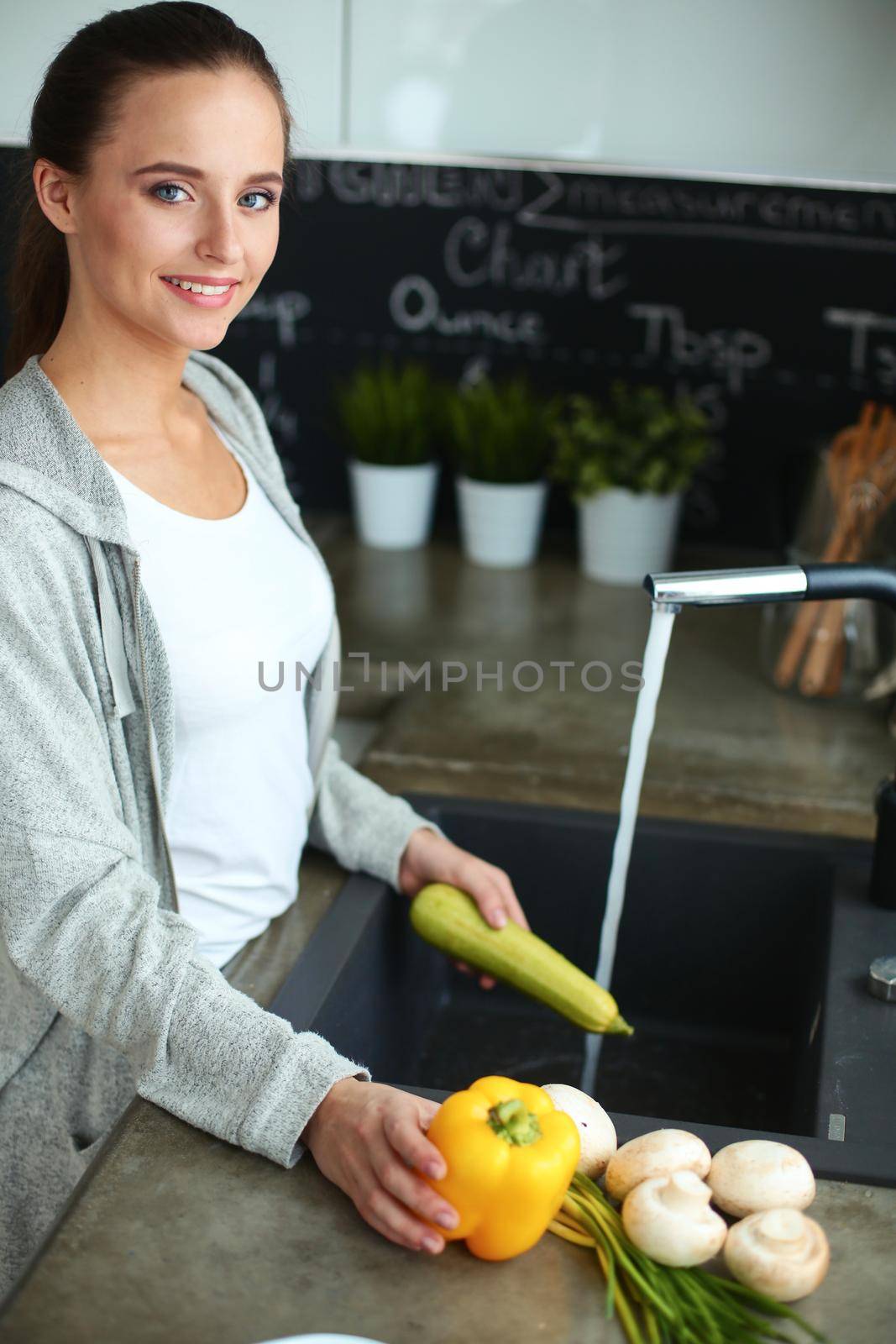 Beautiful young woman washing vegetables for salad while standing in the kitchen.