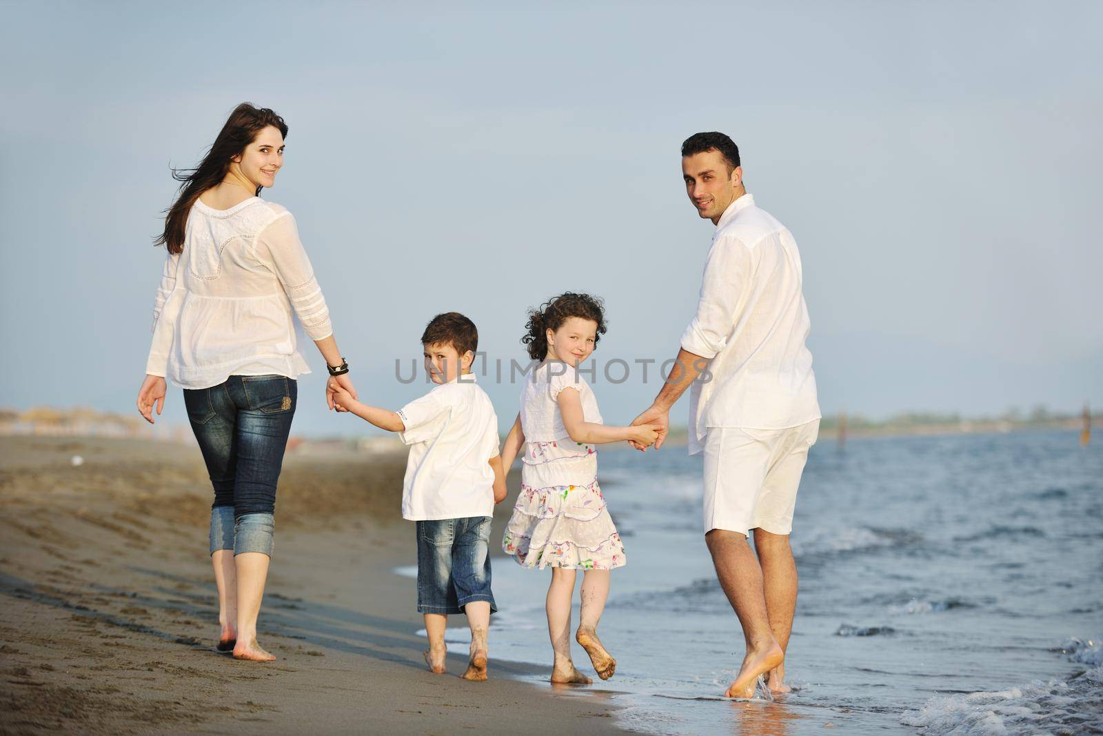 happy young family have fun on beach run and jump  at sunset