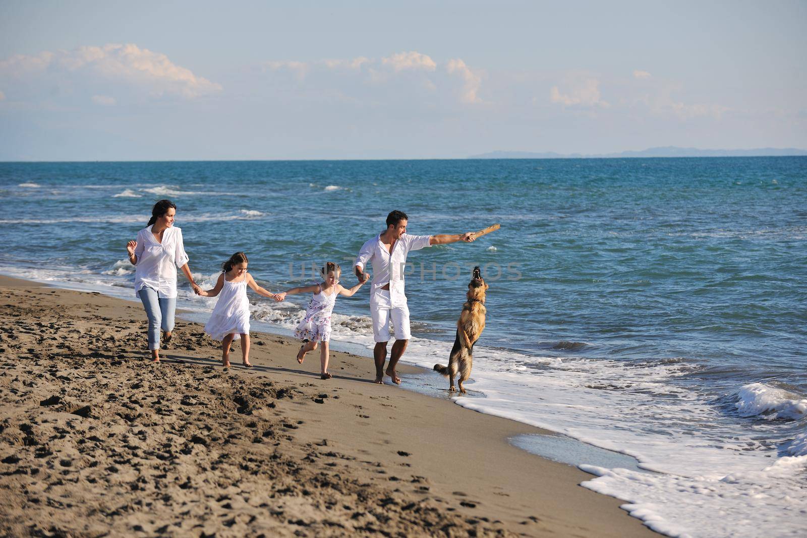 happy young family in white clothing have fun and play with beautiful dog at vacations on beautiful beach 