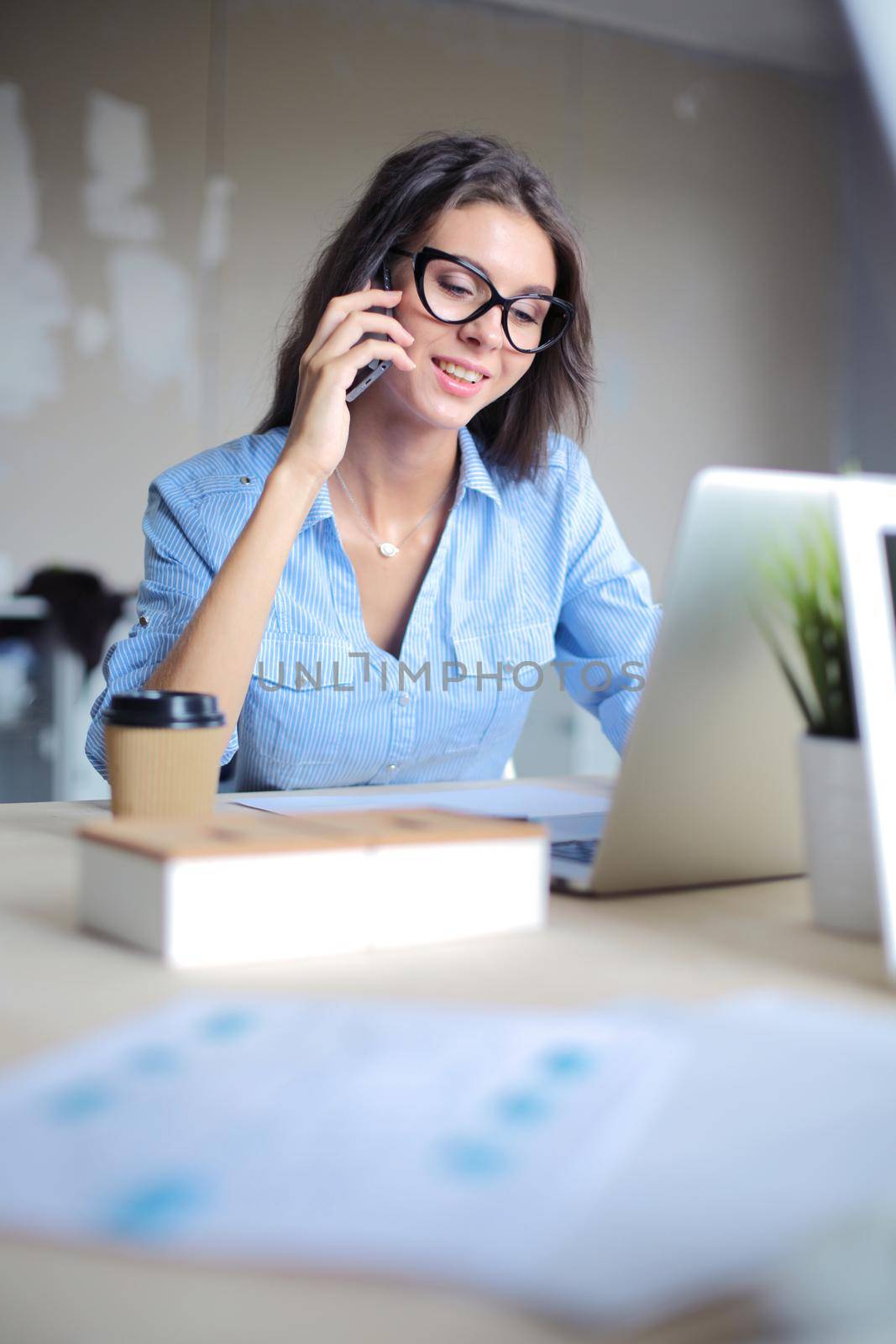 Beautiful young business woman sitting at office desk and talking on cell phone. Business woman by lenetstan