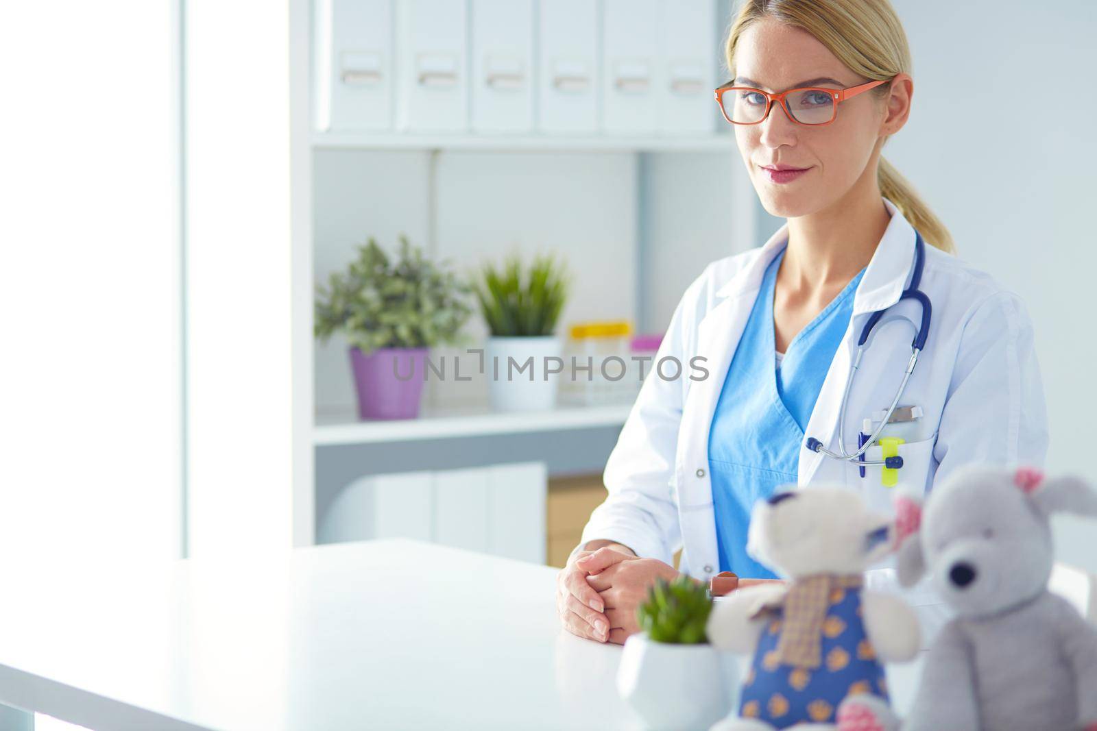 Beautiful young smiling female doctor sitting at the desk. by lenetstan
