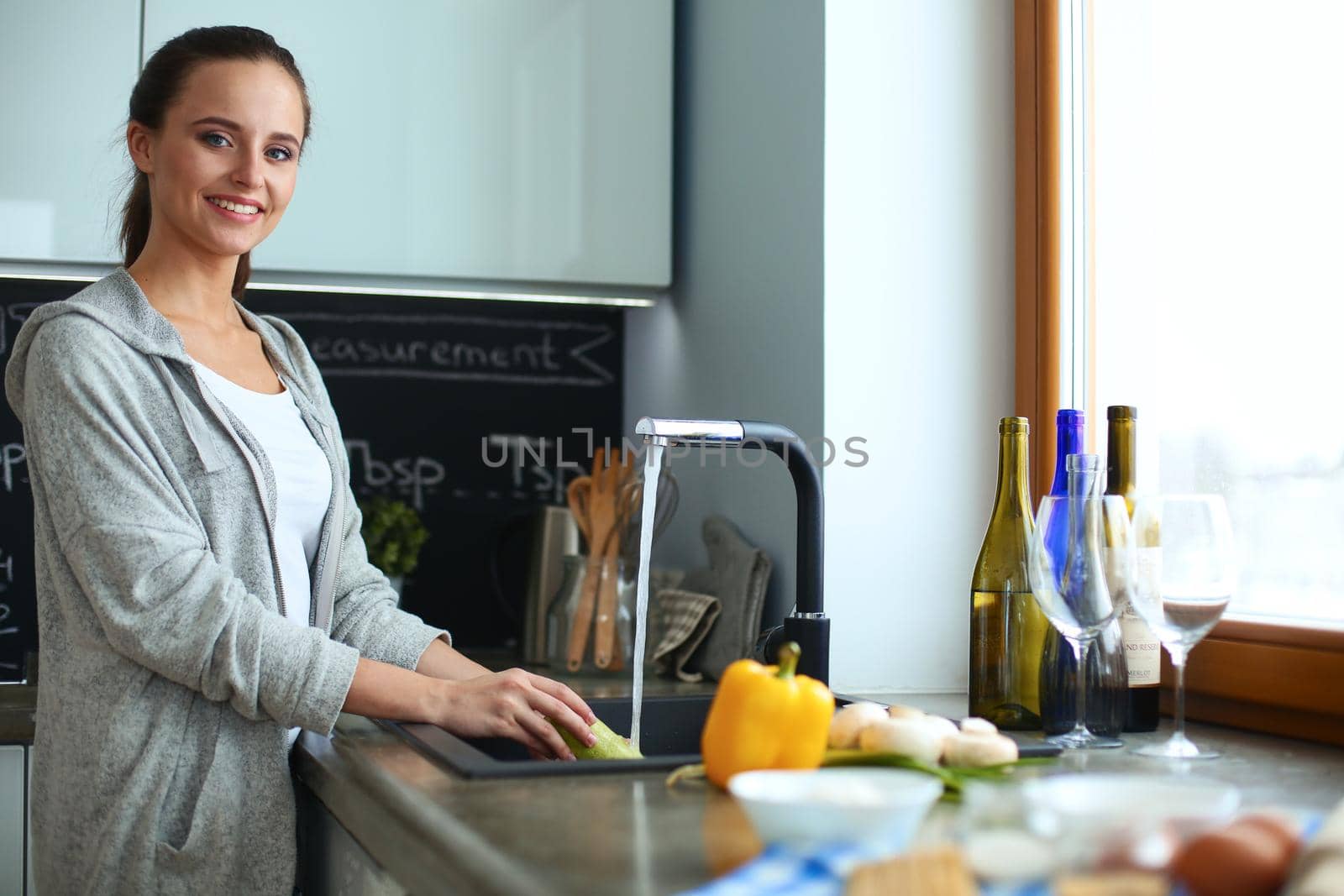 Beautiful young woman washing vegetables for salad while standing in the kitchen by lenetstan