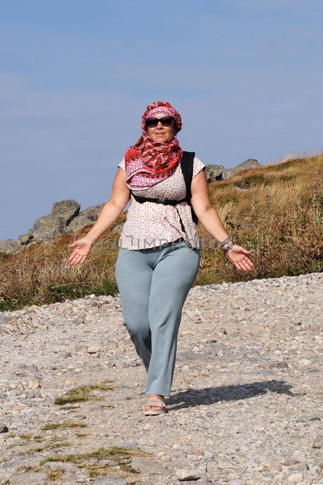 a woman in sunglasses and an arabic headscarf walks along the road under the scorching sun.