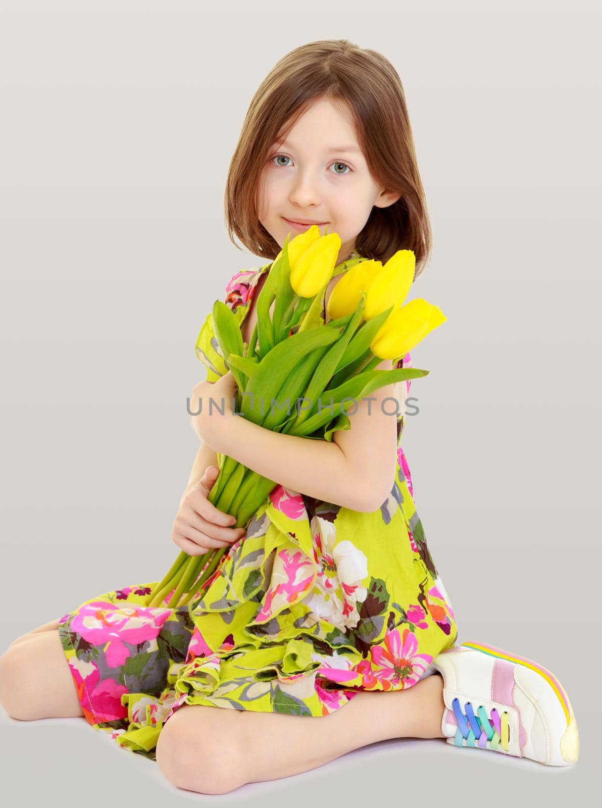 Adorable little Caucasian girl in summer dress holding a bouquet of yellow tulips.On the background of summer blue sky and fluffy clouds.