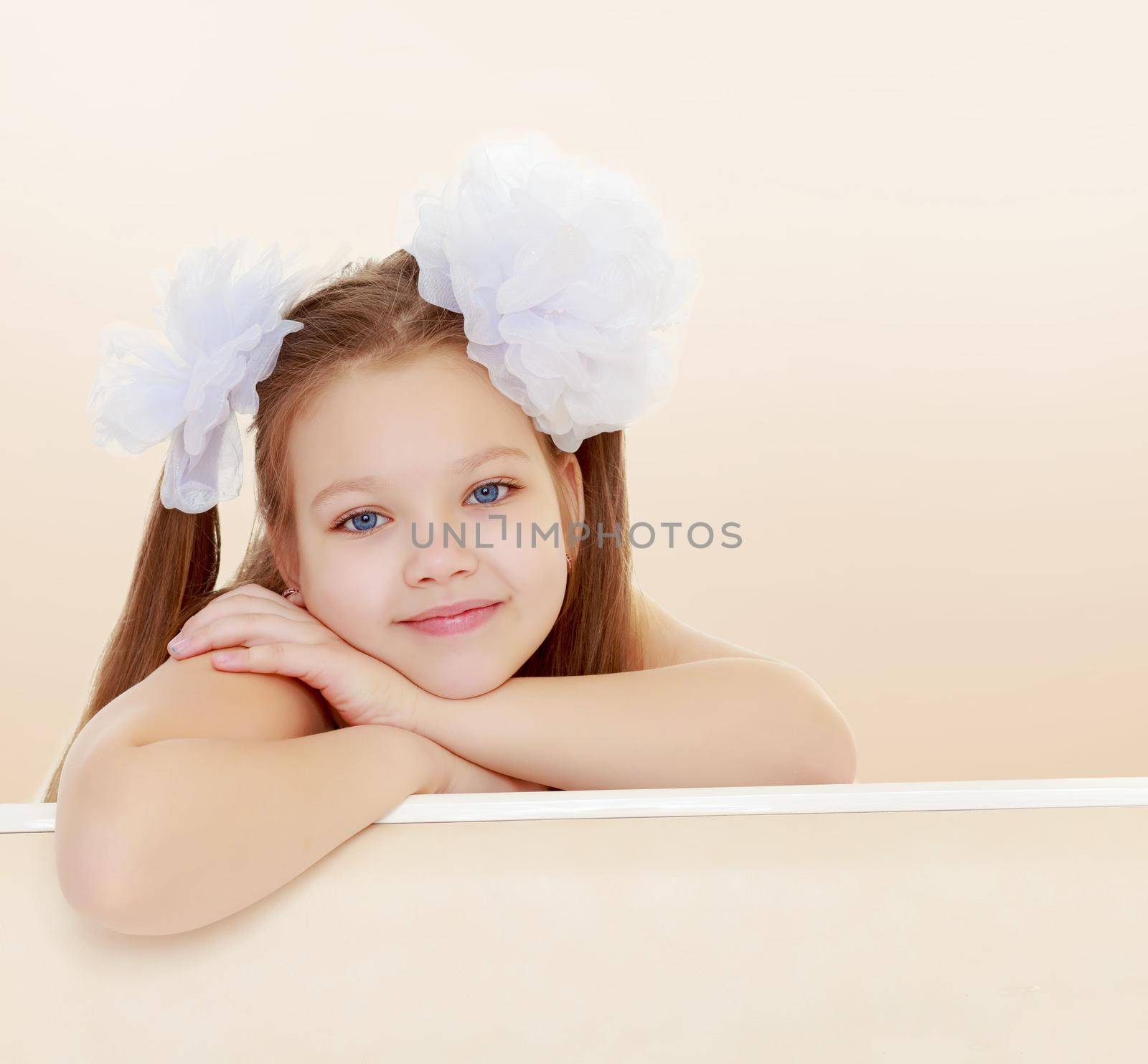 Gentle long-haired little girl with big white bows on the head . She leaned on the windowsill. Close-up.Brown gradient background.