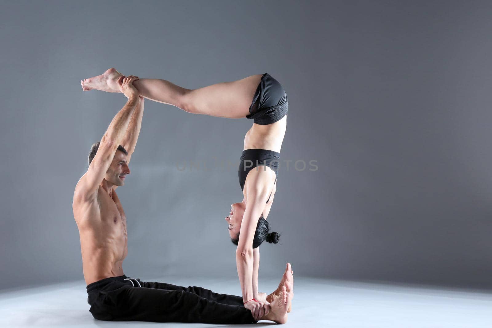 Young couple practicing acro yoga on mat in studio together. Acroyoga. Couple yoga. Partner yoga. by lenetstan