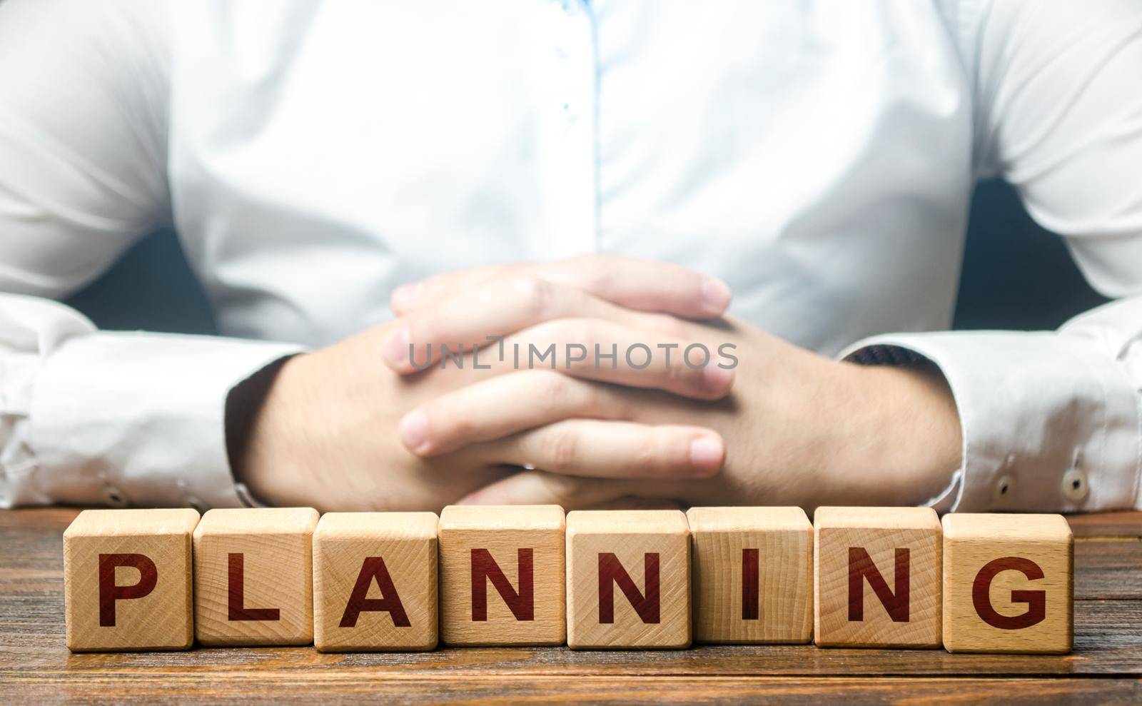 Man folded his hands on a background of blocks with the word Planning. Leadership quality to plan the best options for further action. Provide for any possible consequences. Discretion, determination