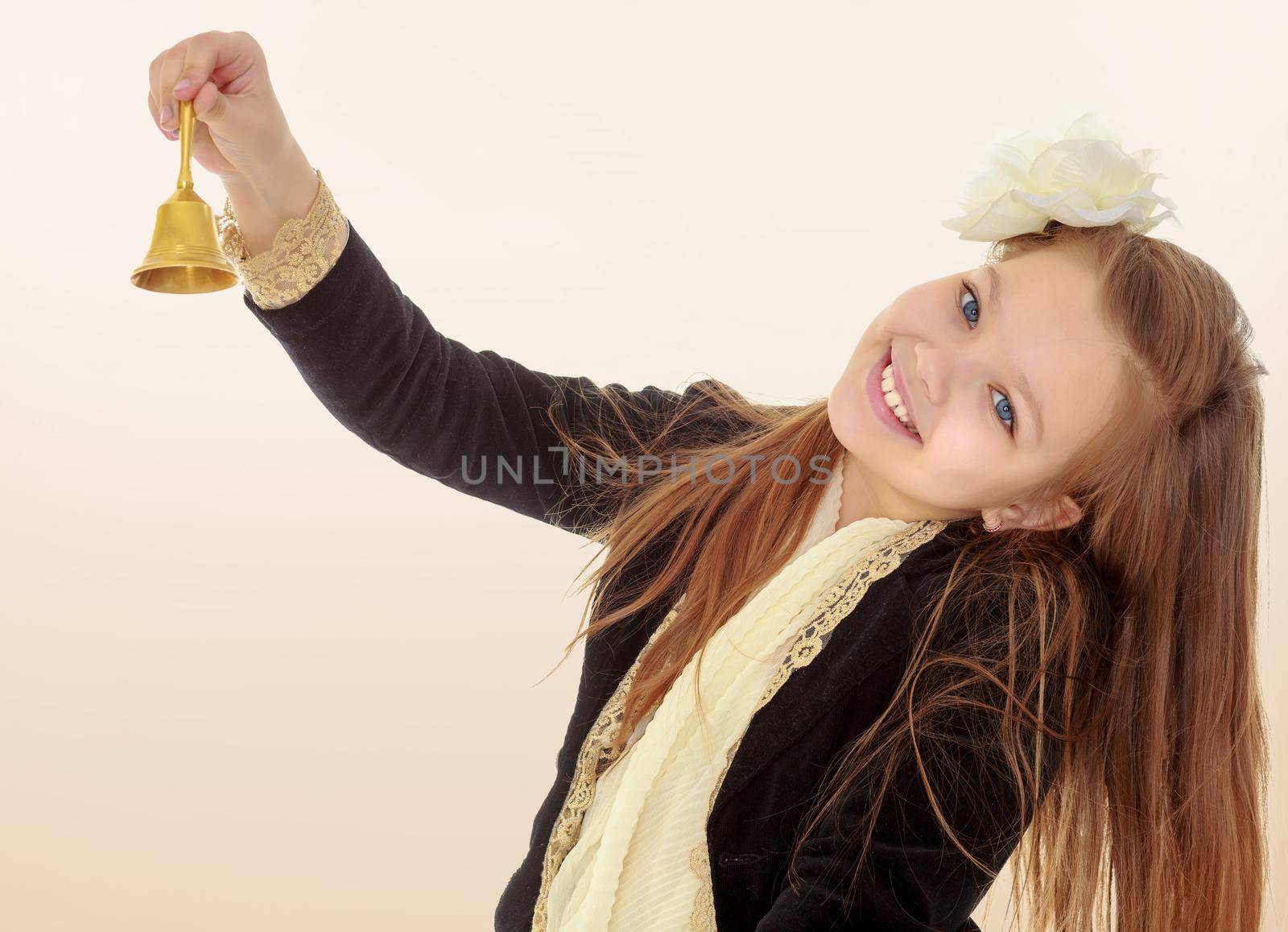 Joyful little long-haired girl with a white rose in her hair, rings the bell. Close-up.Brown gradient background.