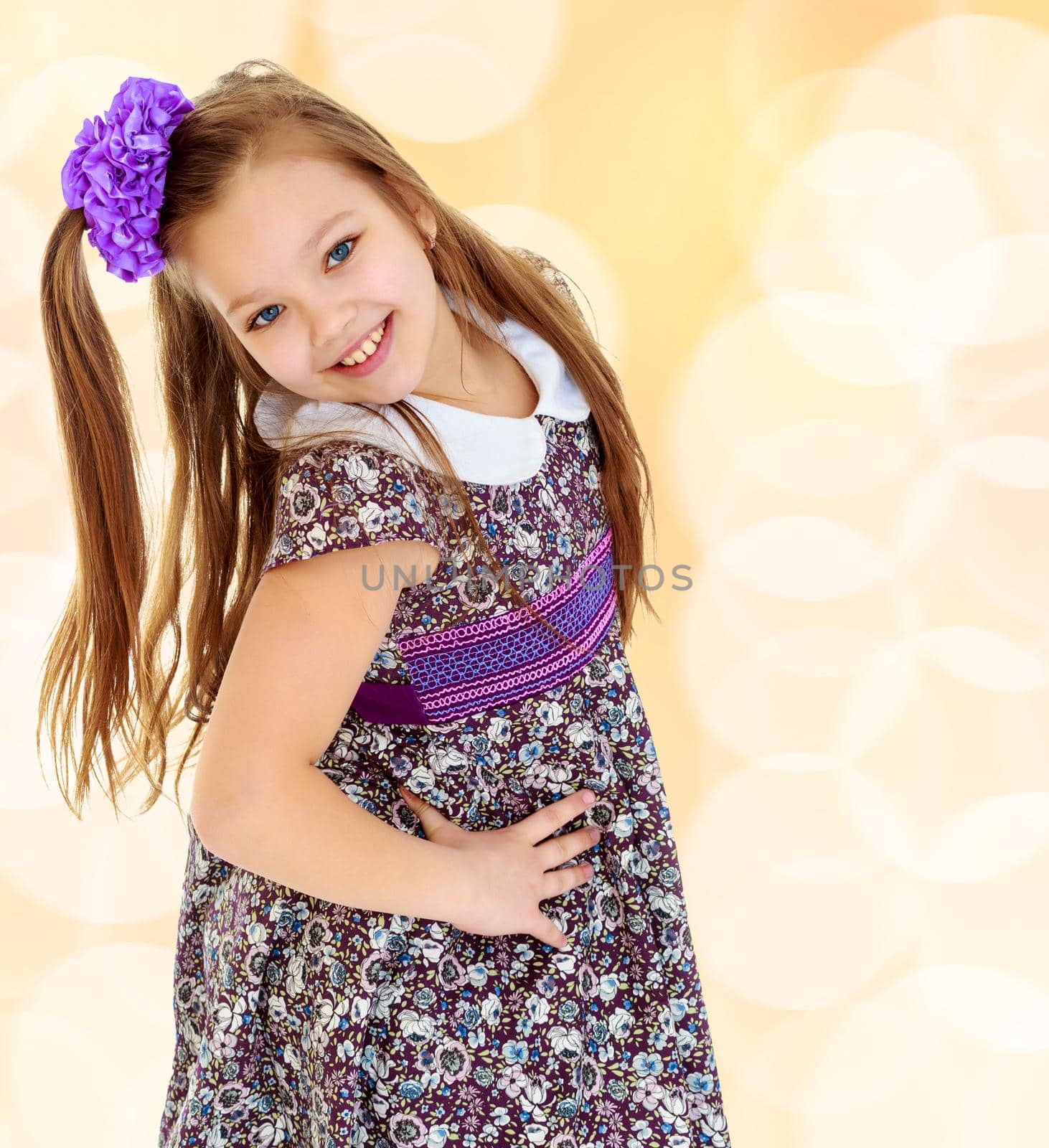 Happy little girl with a big purple bow on her head , and fancy dress. The girl bent her head to see her long beautiful hair.On a brown blurred background with white snowflakes.