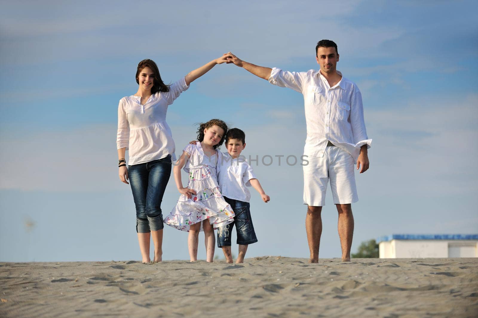 happy young family have fun on beachand showing home sign with conncected hands while protecting childrens