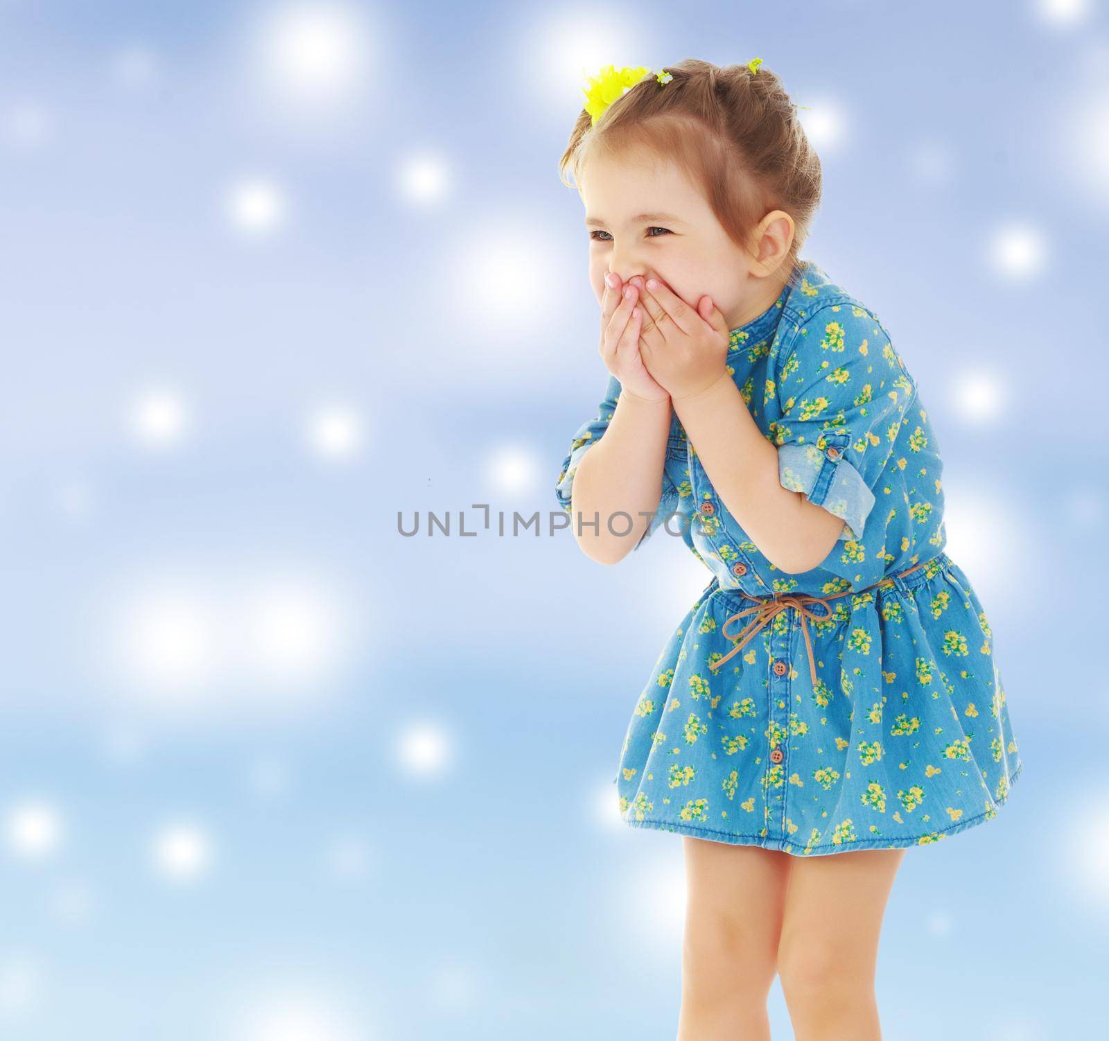 Cute little girl in a short blue dress terrified has closed hands the person. Close-up.Gentle blue Christmas background with white snowflakes abstract.