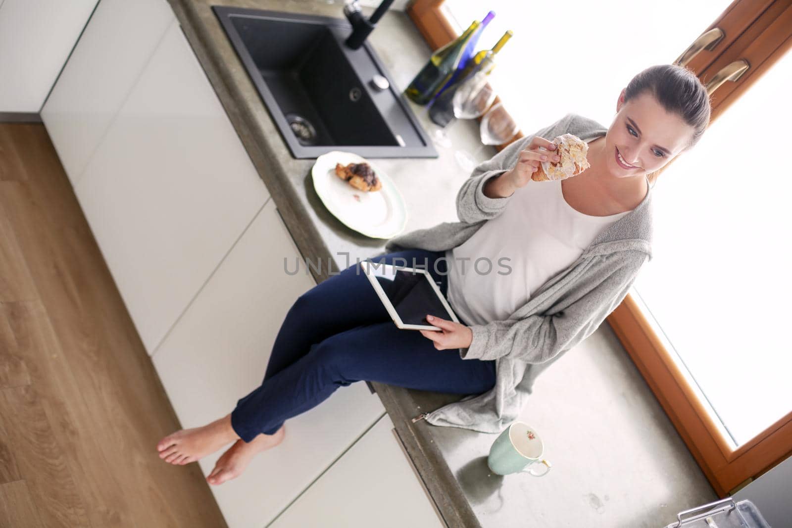 Beautiful young woman using a digital tablet in the kitchen