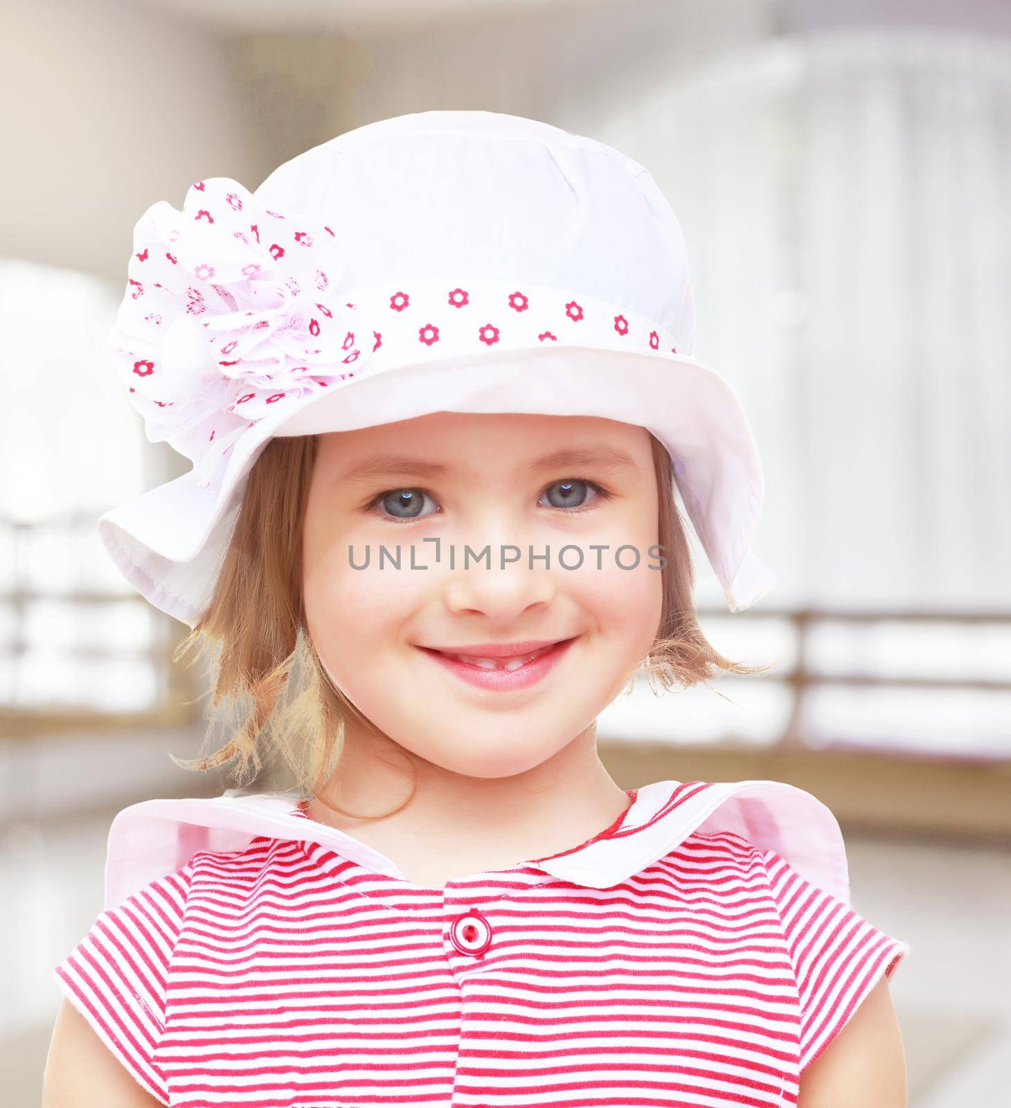 Portrait of beautiful little blond girl in a white hat with a pink bow. Close-up.On the background of the hall with a large arched window , the concept of learning and child development.