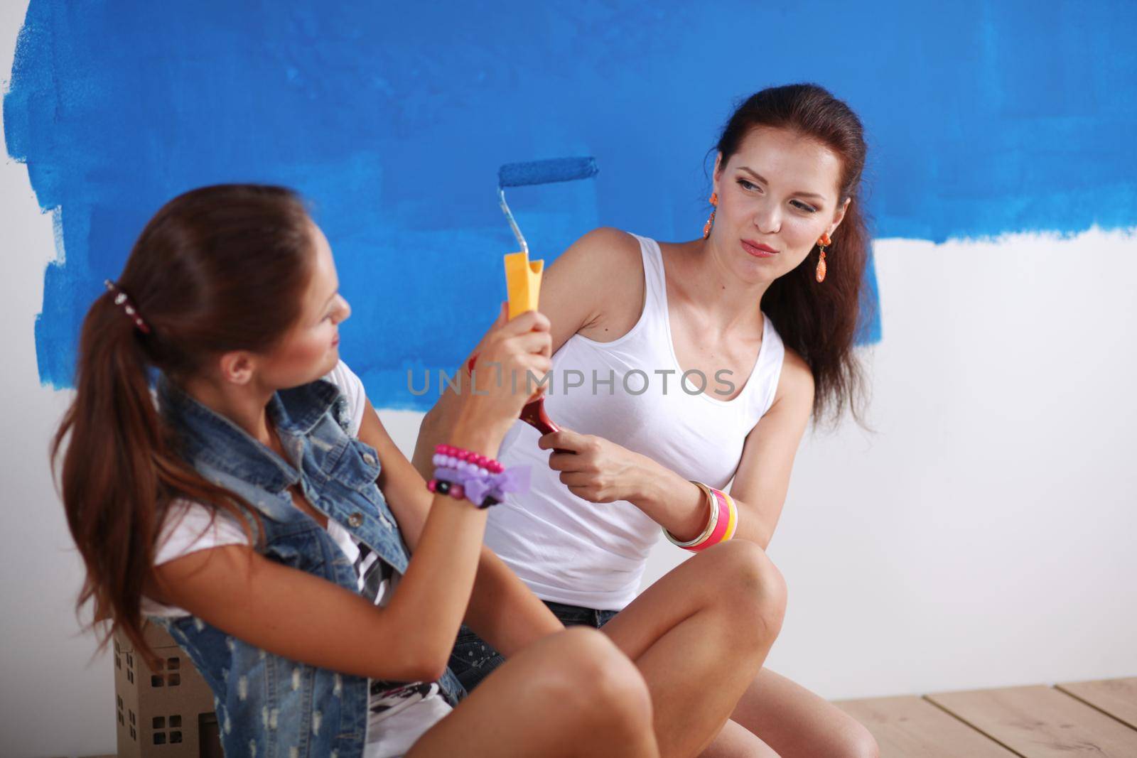 Two Beautiful young woman doing wall painting, sitting. Two Beautiful young woman