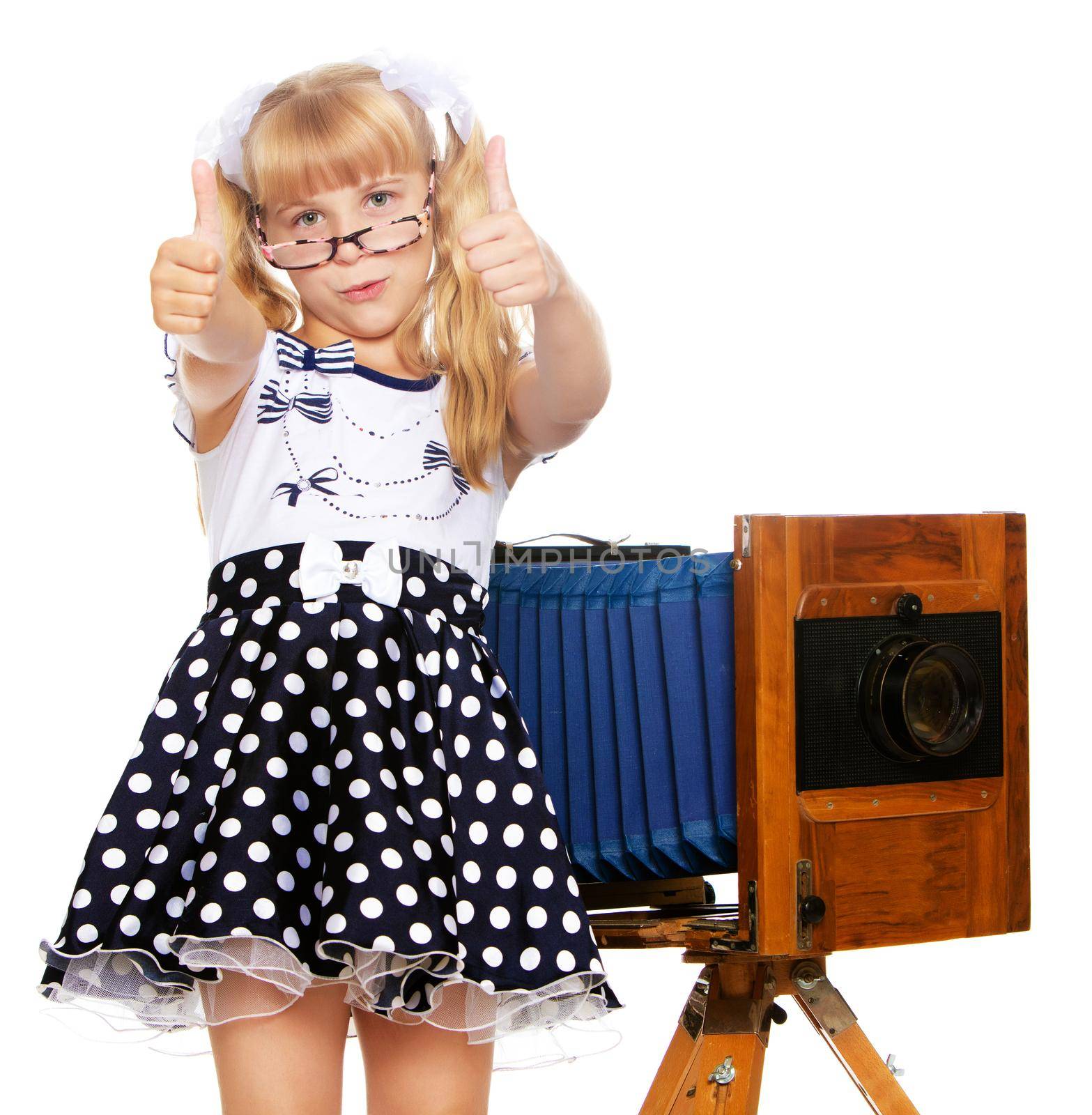 Adorable little blond girl wearing glasses and fancy dress polka dot advertises the old wooden camera-Isolated on white background