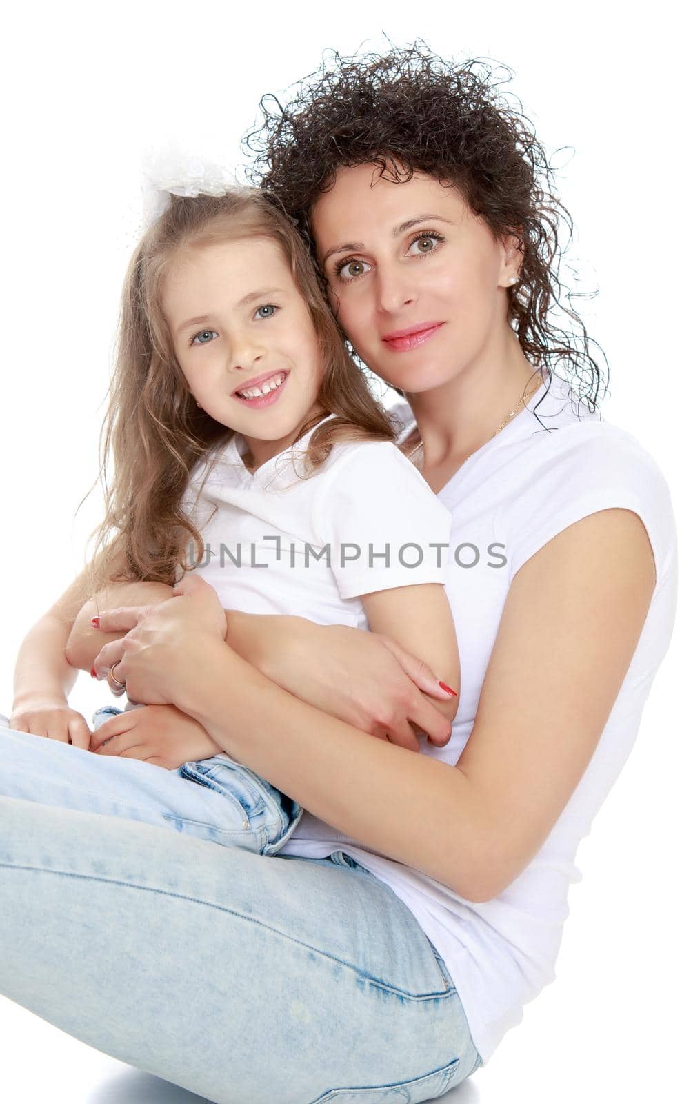 Happy, charming young mother with adorable little daughter. In the same jeans and white t-shirts without a pattern. Mom sits on floor and holds daughter on hands - Isolated