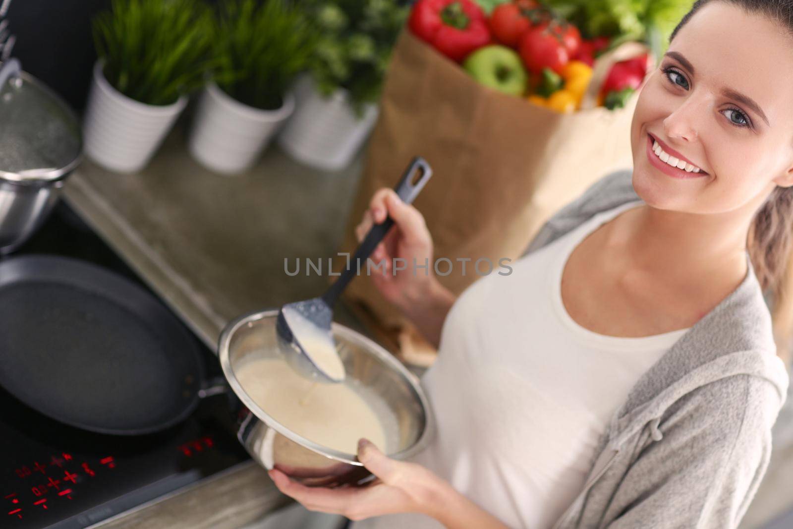 Young woman prepares pancakes in the kitchen while standing near the table. Woman in the kitchen. Cooking at kitchen. by lenetstan