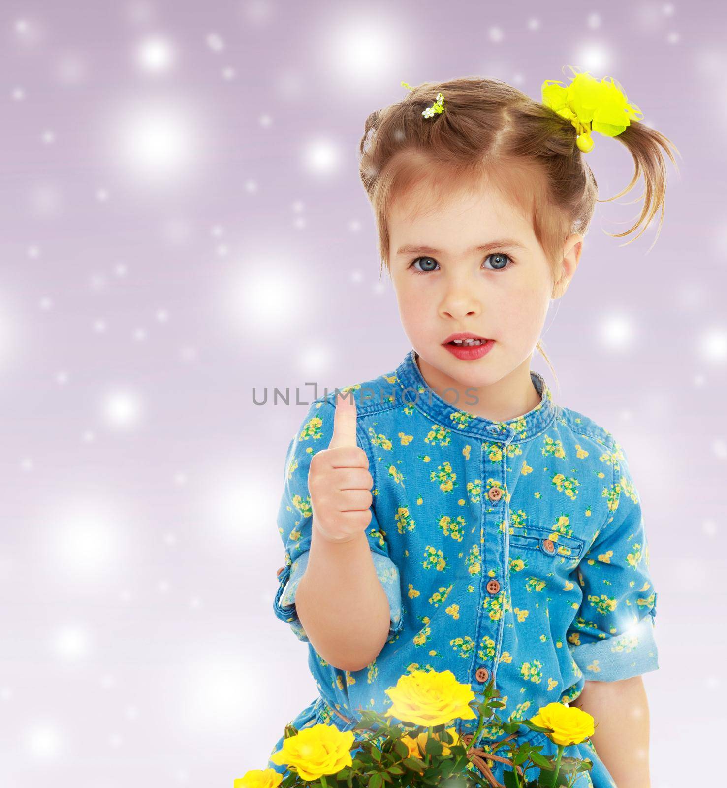 Cute little girl in a blue dress. The girl shows the thumb of the right hand. Before her a bouquet of yellow flowers.On new year purple background with white snowflakes.