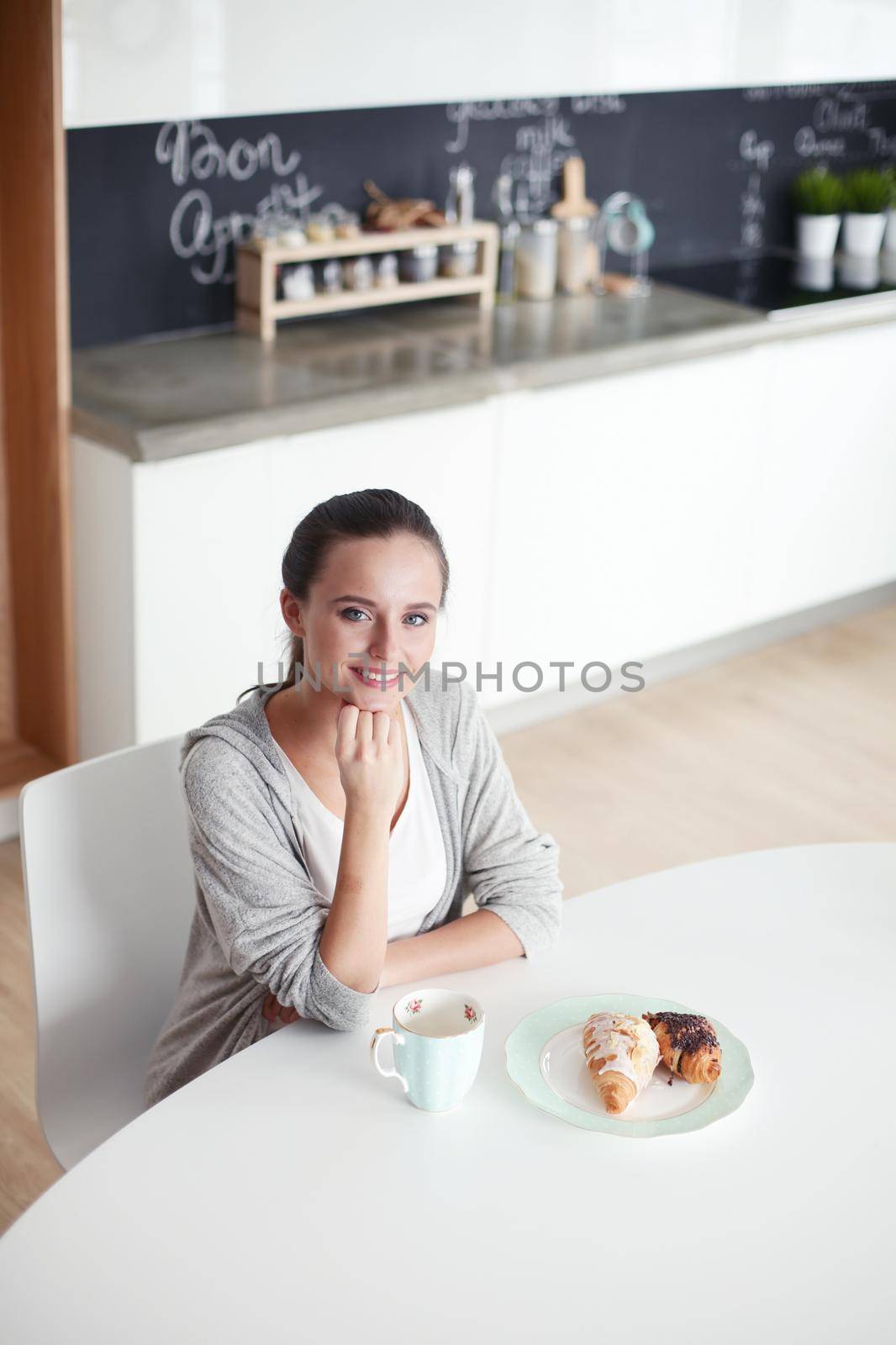Woman drinking tea with sweet croissant at the kitchen table. by lenetstan