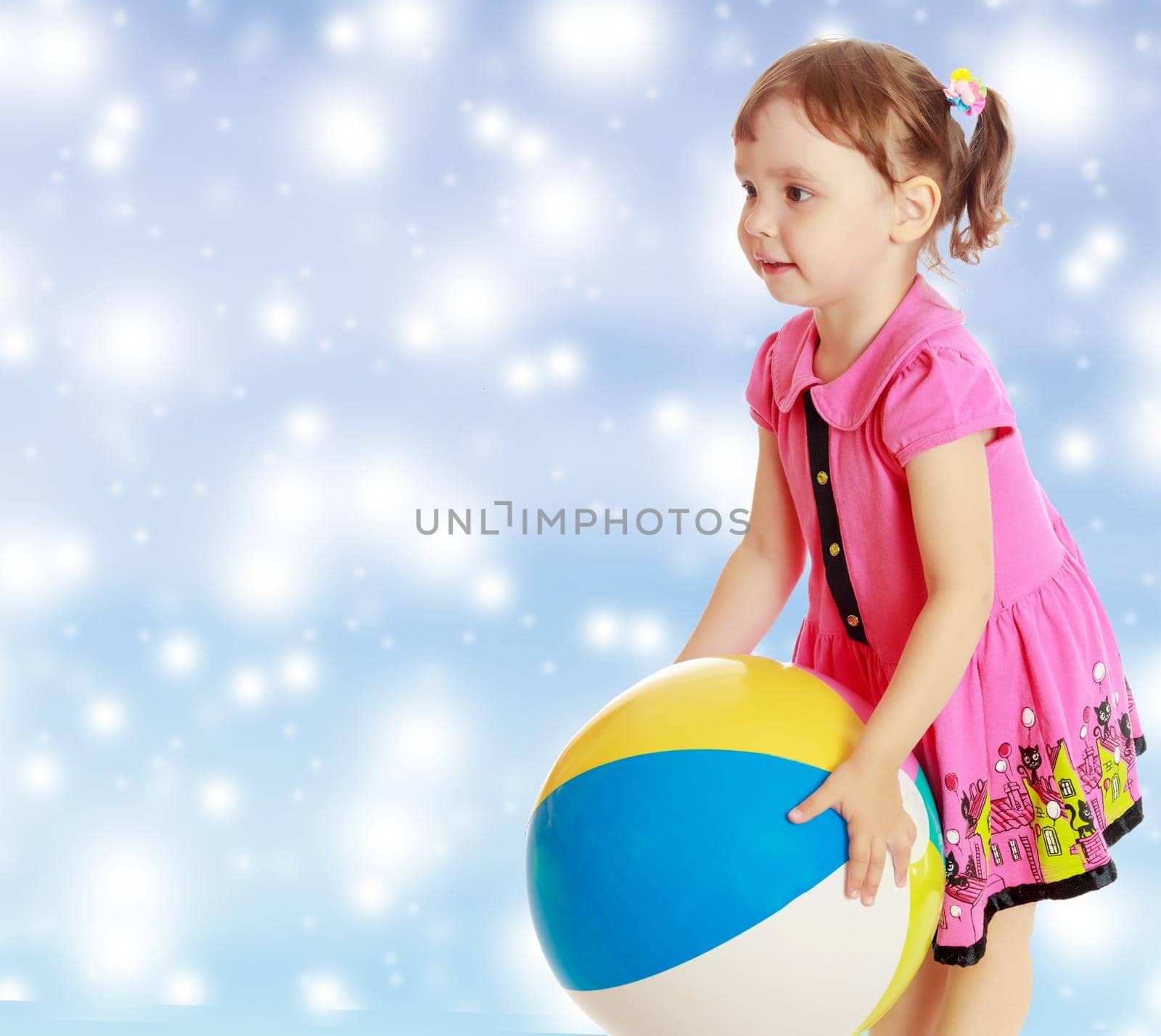 Beautiful little girl in a pink dress throwing a big striped ball. Turned sideways. Close-up.On new year or Christmas blue background with white big stars.