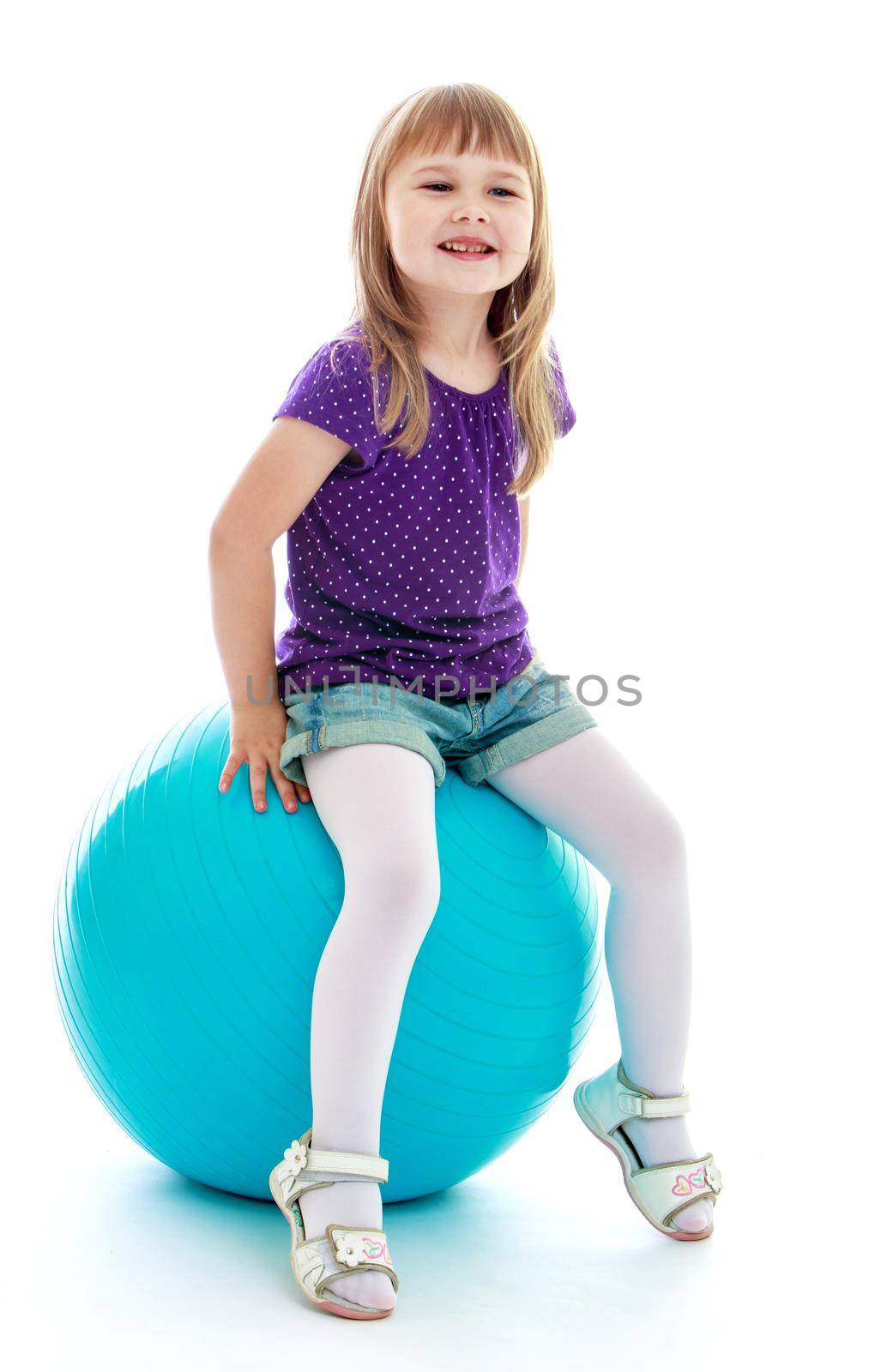 charming little girl in blue shorts playing with a big blue ball. Happy childhood, fashion, autumnal mood concept. Isolated on white background