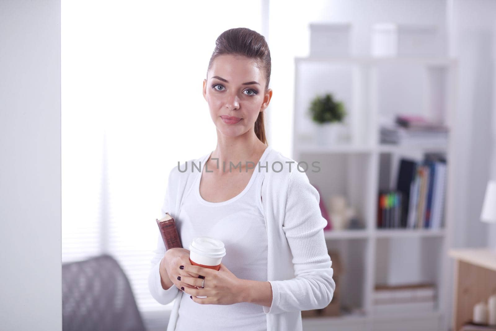 Attractive businesswoman standing near wall in office with book. by lenetstan