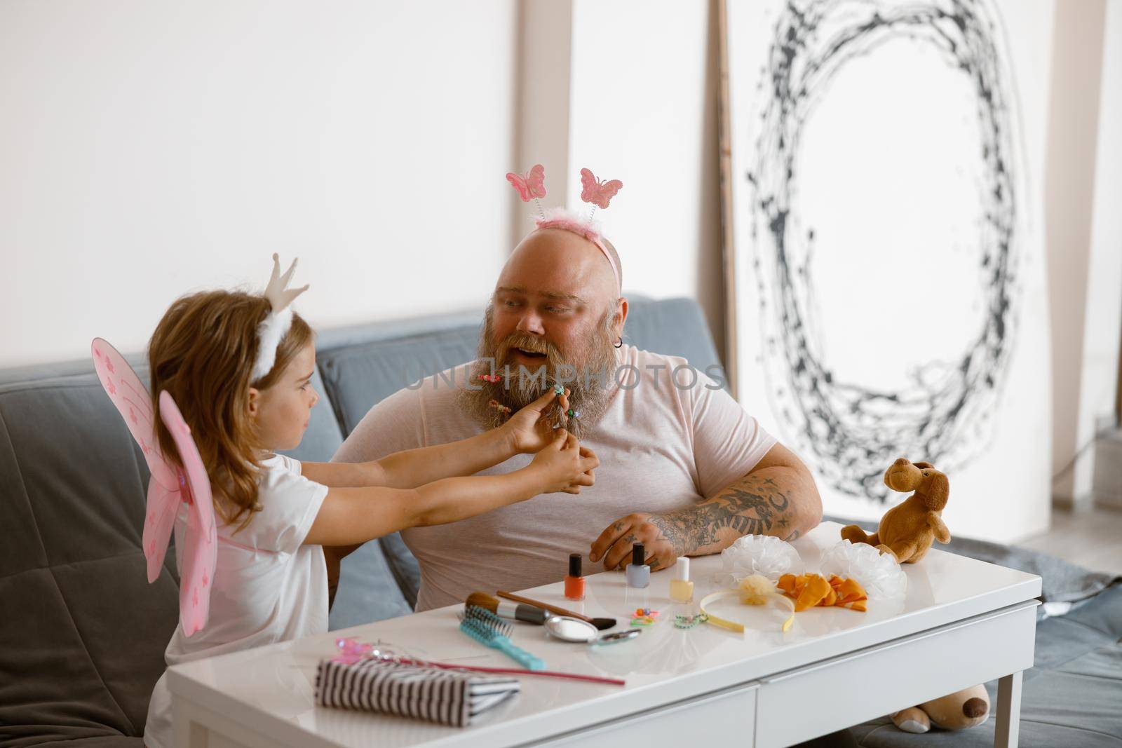 Happy father plays beauty salon with little girl wearing fairy suit at home by friendsstock