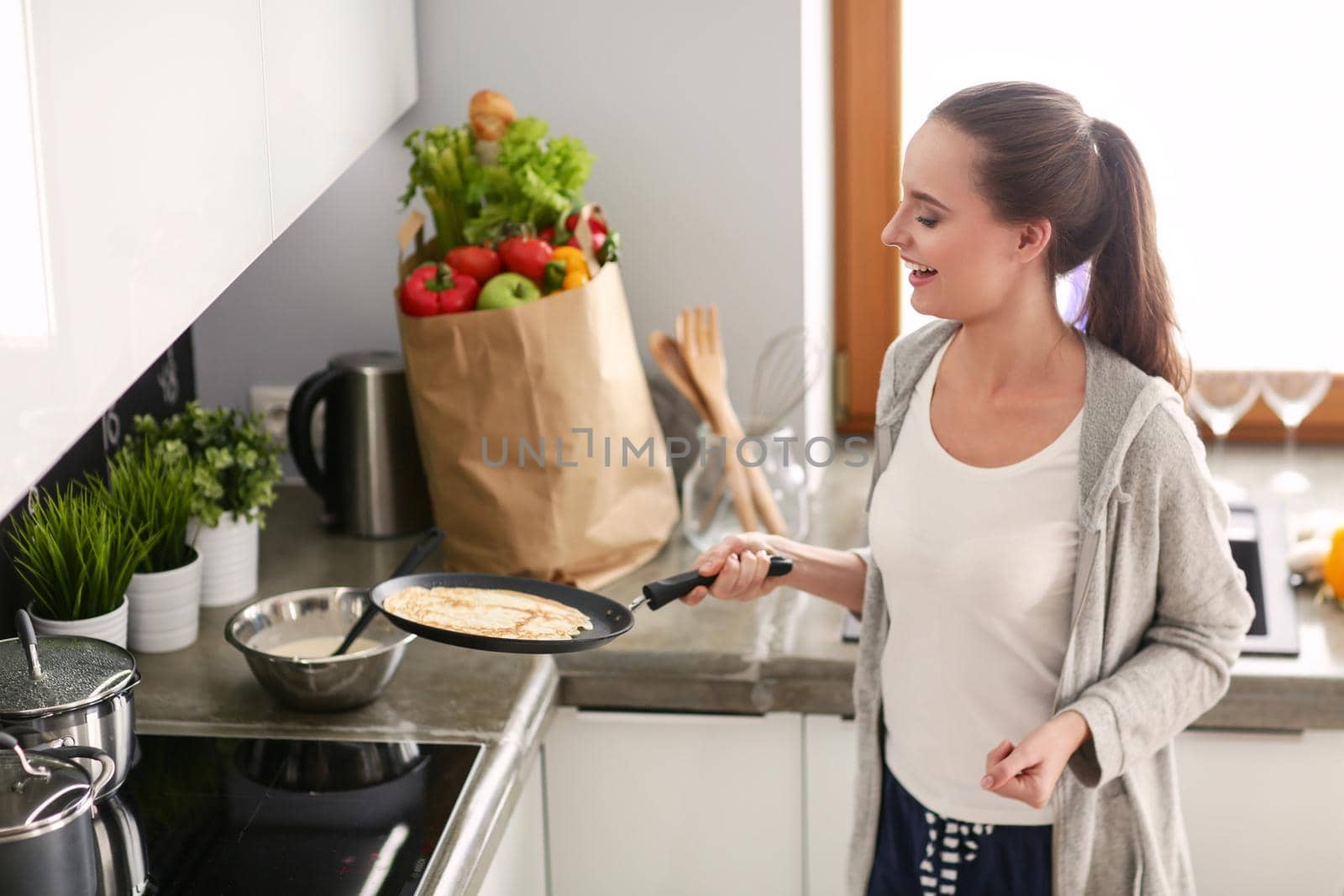 Young woman prepares pancakes in the kitchen while standing near the table. Woman in the kitchen. Cooking at kitchen