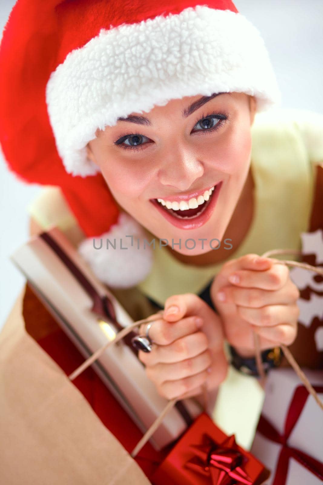 Smiling woman in santa hat with many gift boxes on white background.