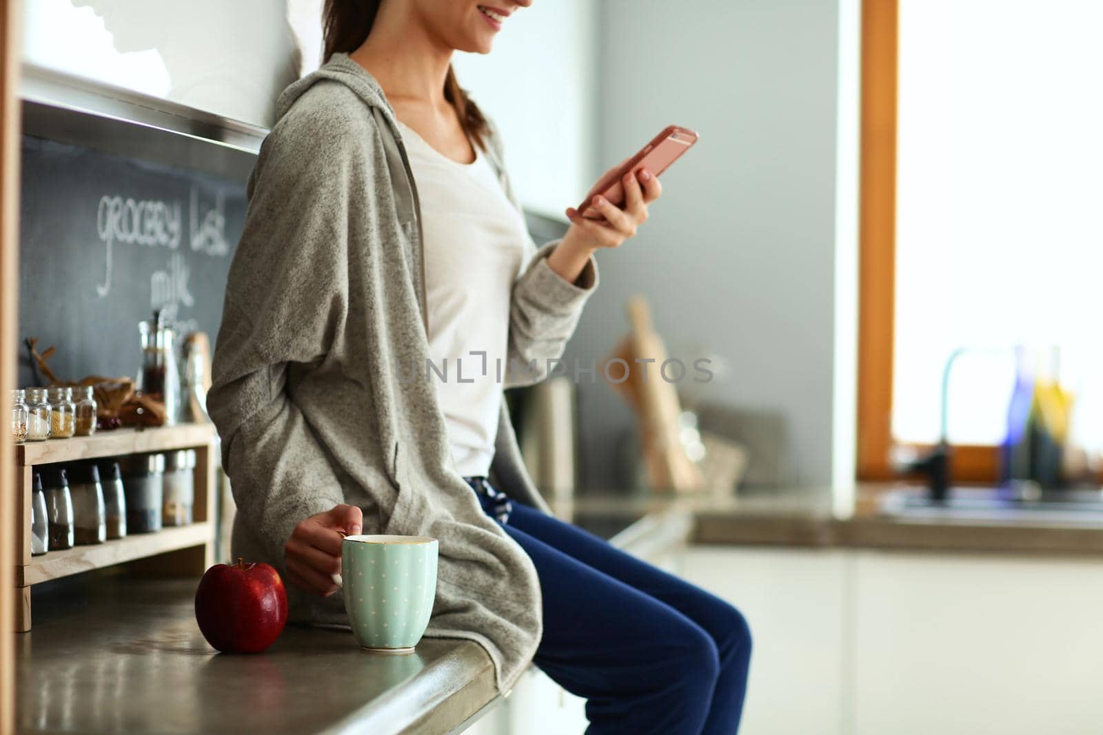 Woman using mobile phone sitting in modern kitchen.