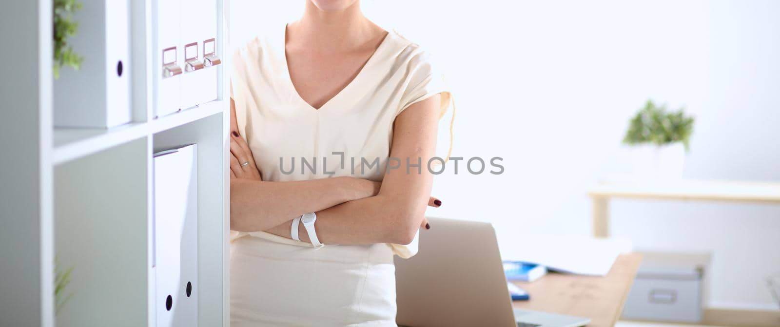 Attractive businesswoman standing near wall in office .