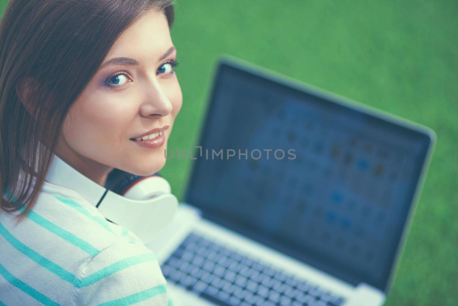 Young woman with laptop sitting on green grass.