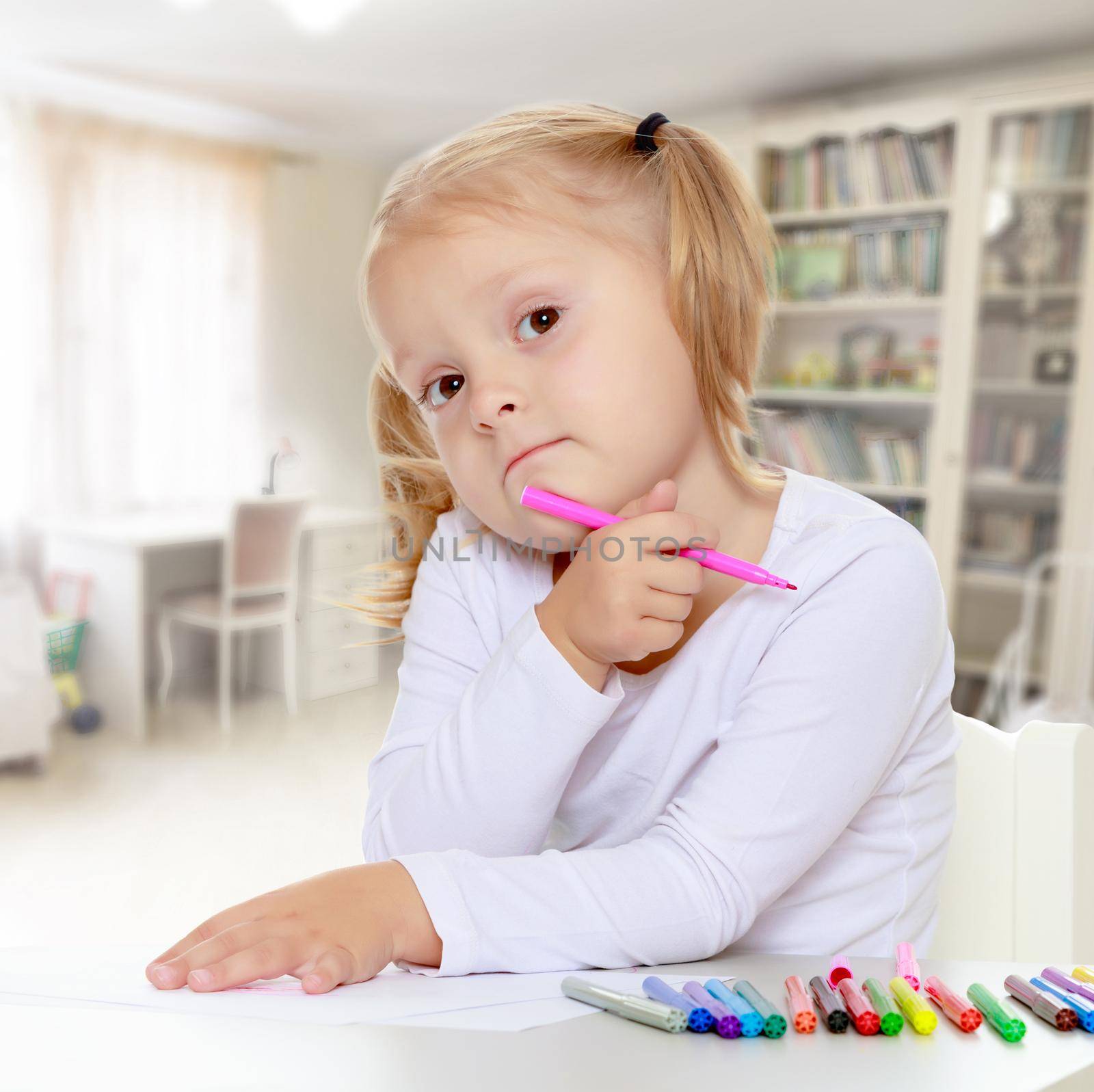 The concept of family happiness,and preschool education of the child , against a child's room with bookshelves.Pretty little blonde girl drawing with markers at the table.