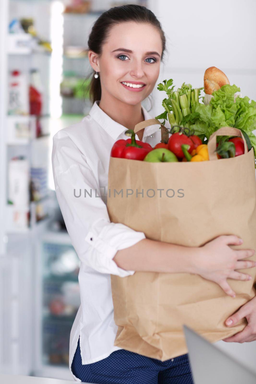 Young woman holding grocery shopping bag with vegetables .Standing in the kitchen. Woman in the kitchen looking at the camera by lenetstan