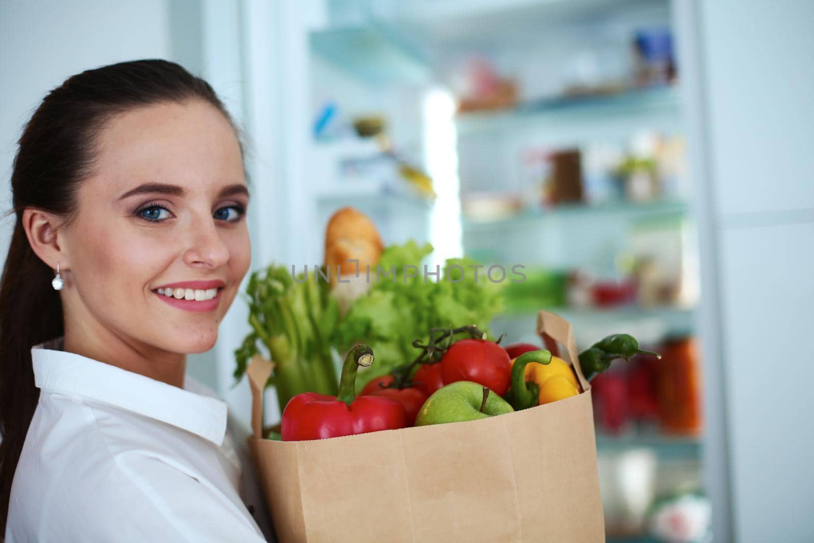 Young woman holding grocery shopping bag with vegetables .Standing in the kitchen.