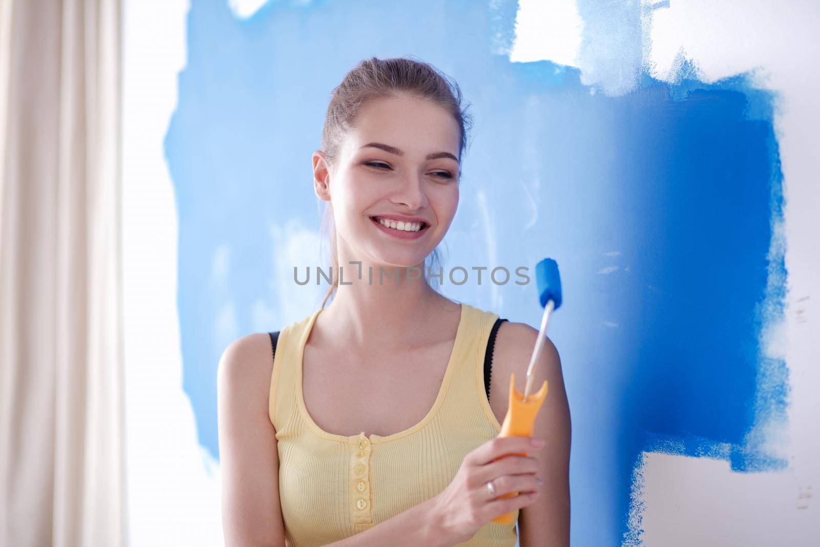 Beautiful young woman doing wall painting, standing .