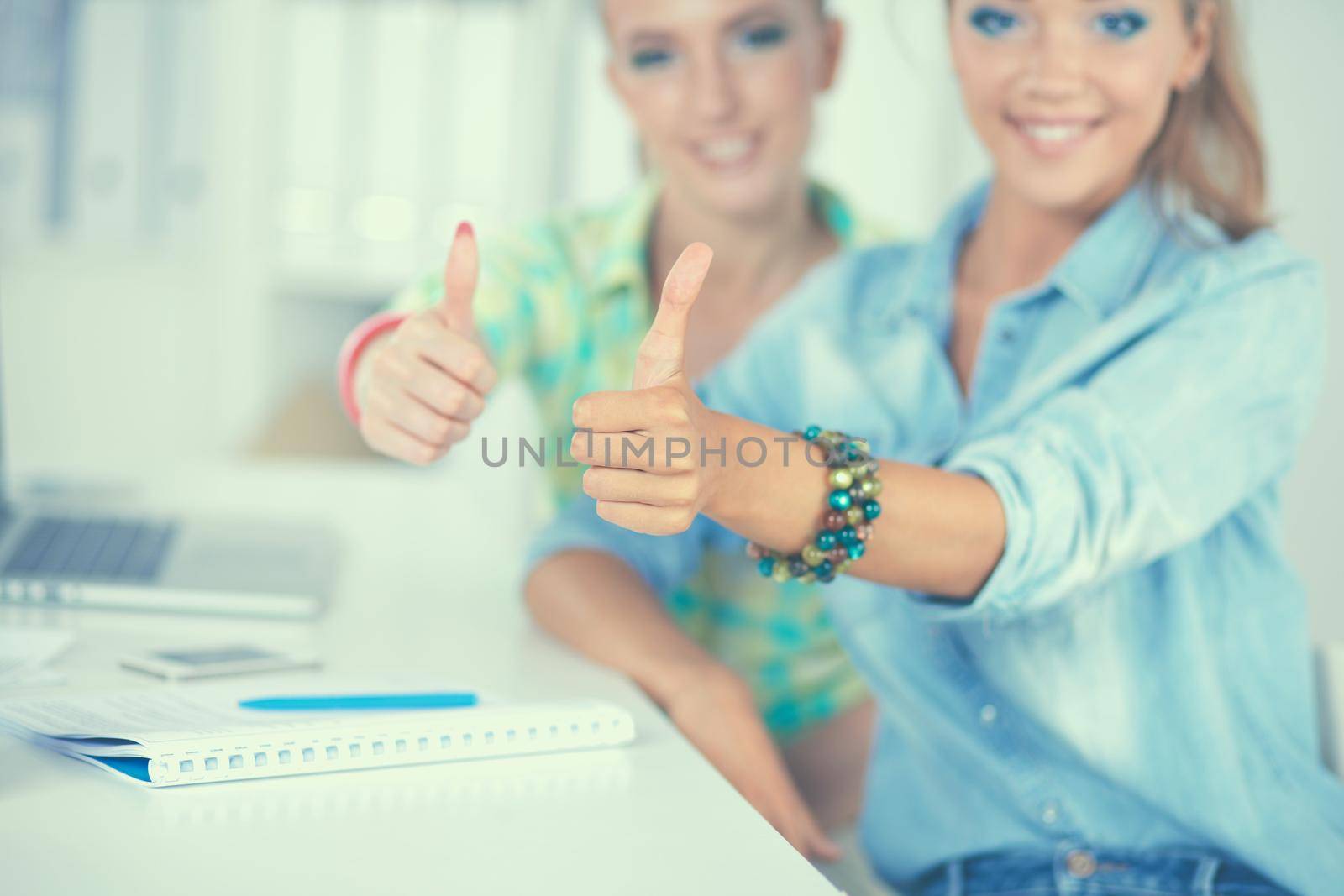 Two women working together at office, sitting on the desk.