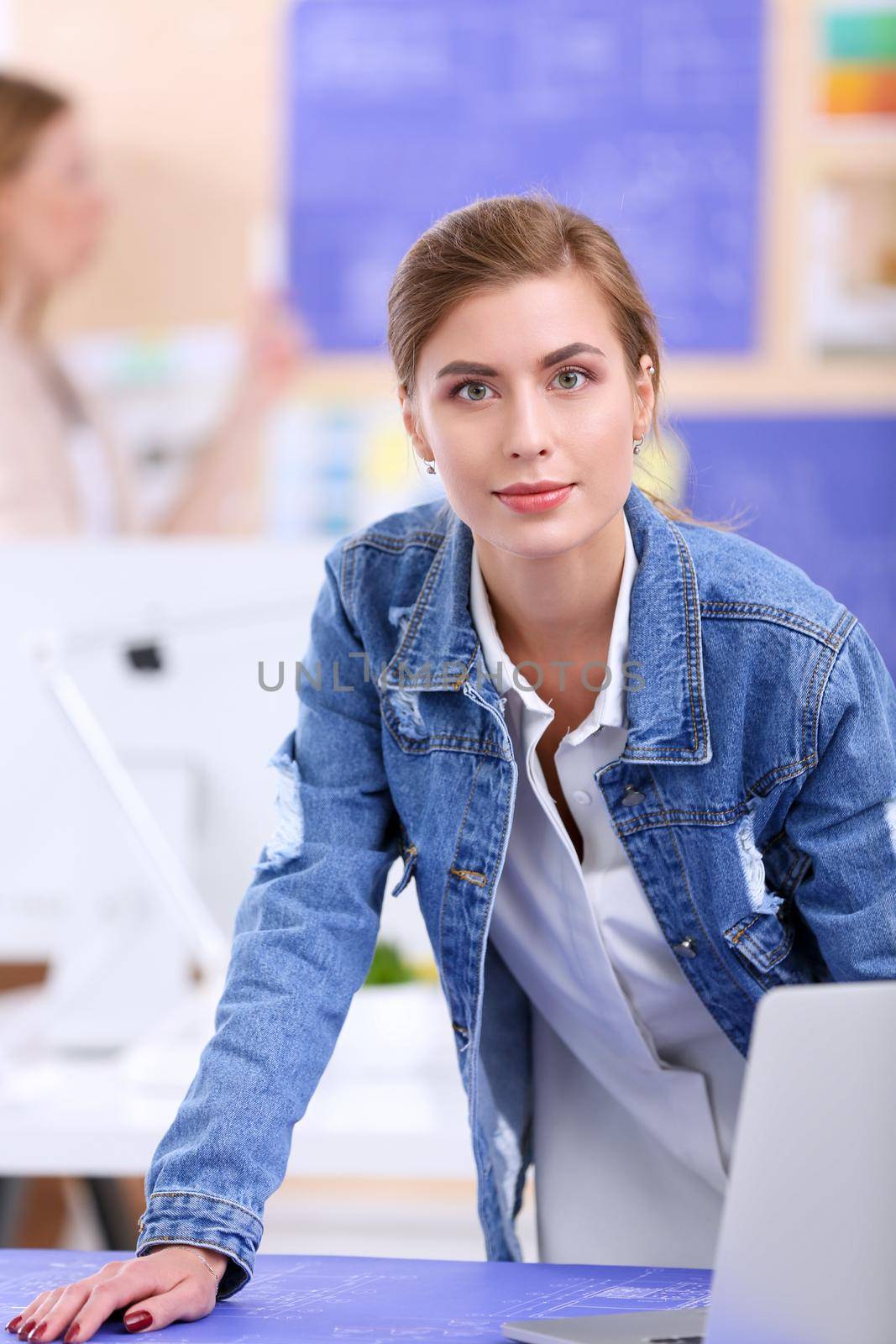 Two young woman standing near desk with instruments, plan and laptop